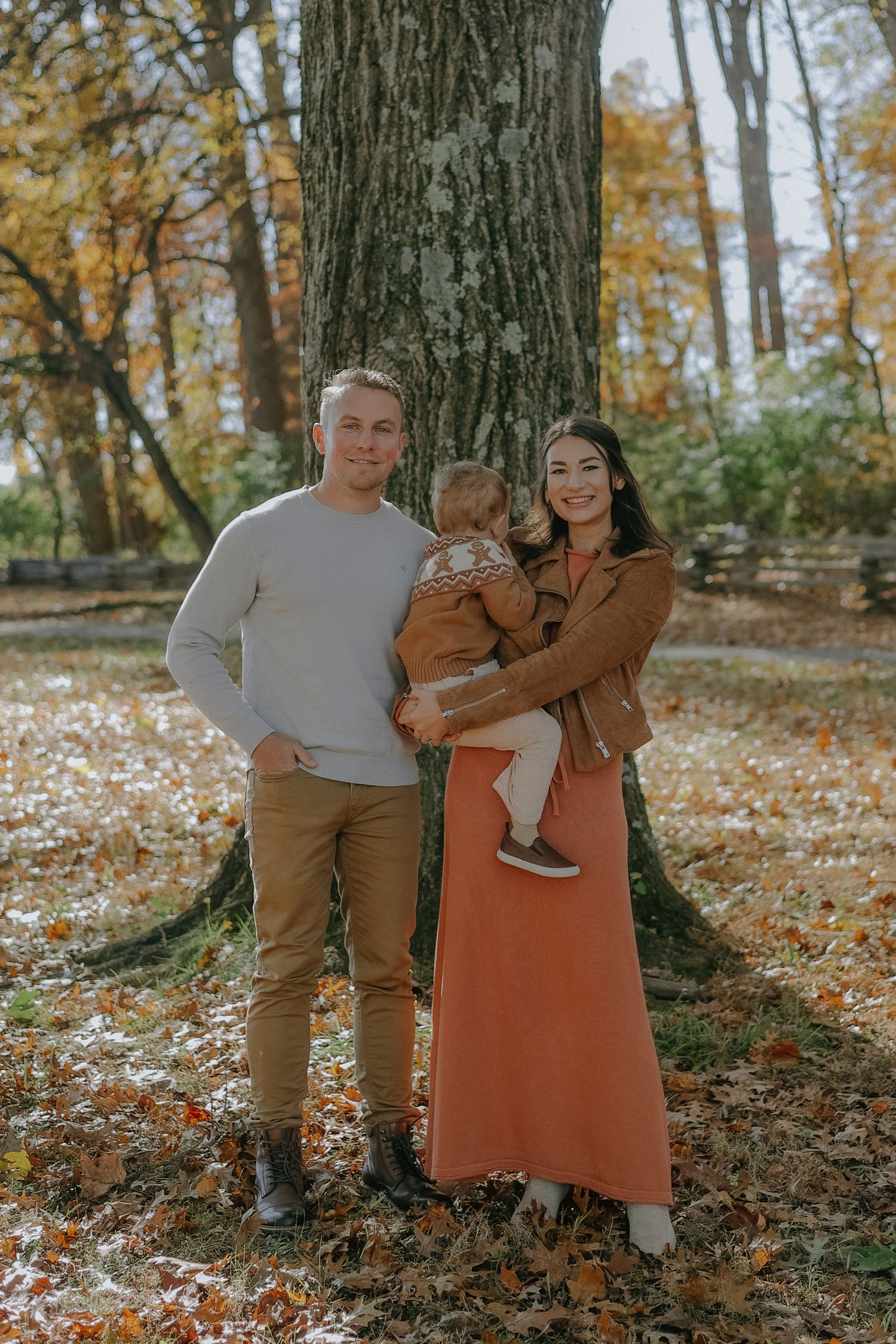 Family enjoying autumn day in forest with fallen leaves and sunlit trees in background.
