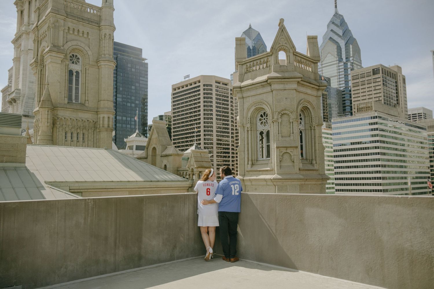Couple poses in front of a grand cathedral with city skyline visible in the background.