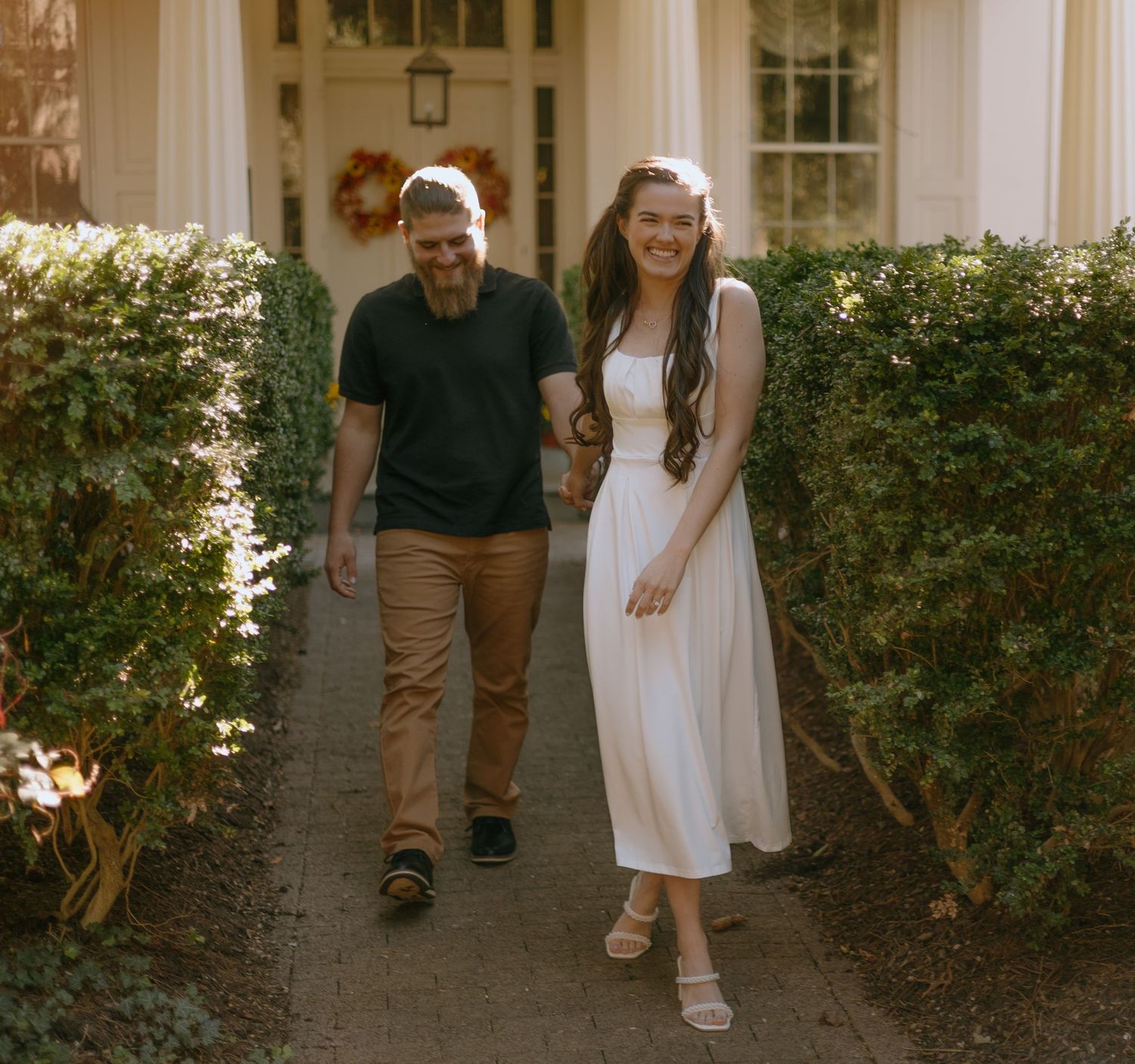 A couple walking together on a garden path wearing casual attire in warm sunlight.
