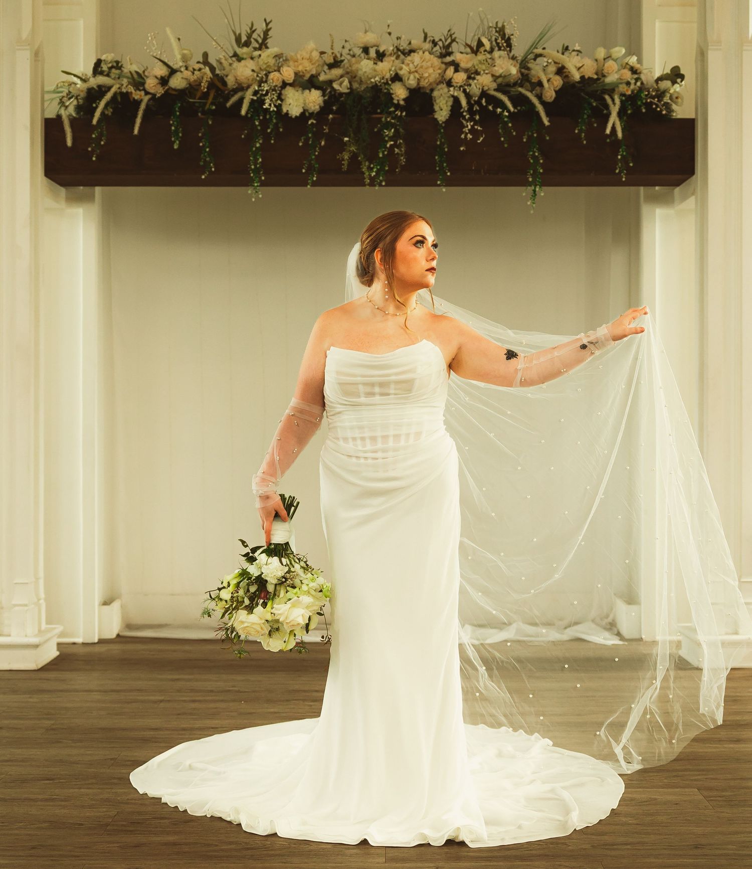 A flowing white wedding dress photographed in an elegant venue with floral decorations.