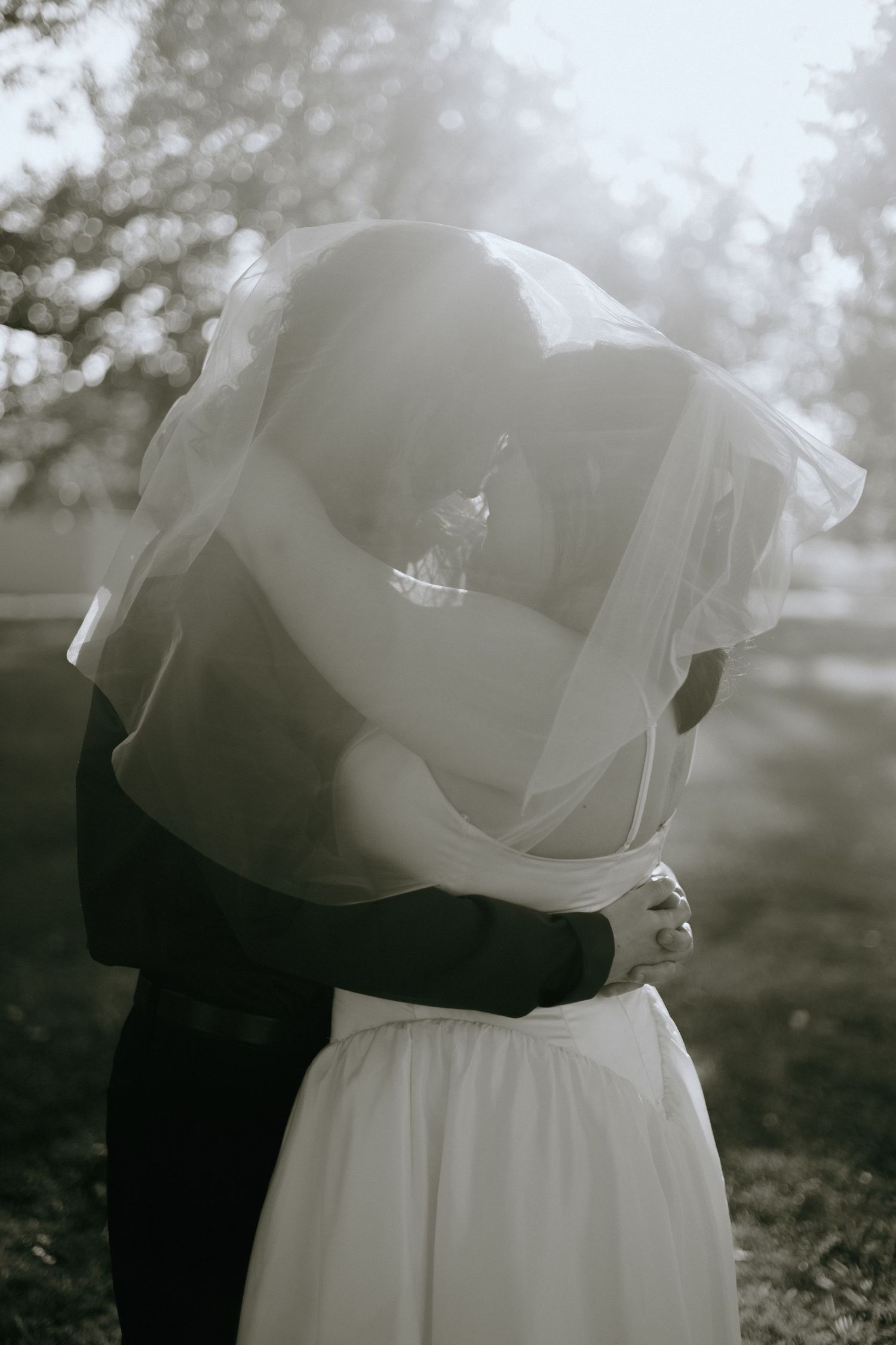 An artistic black and white photo of a couple embracing with a flowing veil in soft focus.