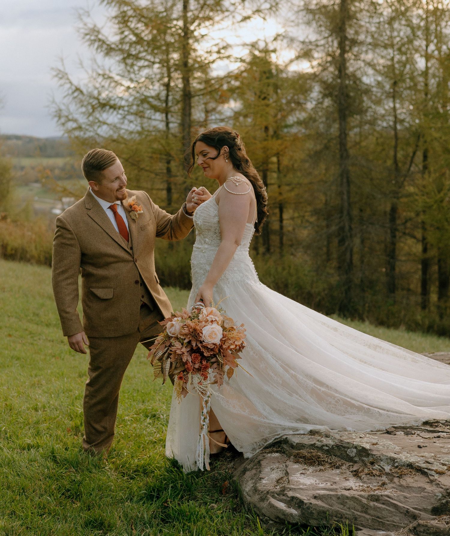 Wedding couple posing with flowing veil on fallen tree trunk in mountain setting.
