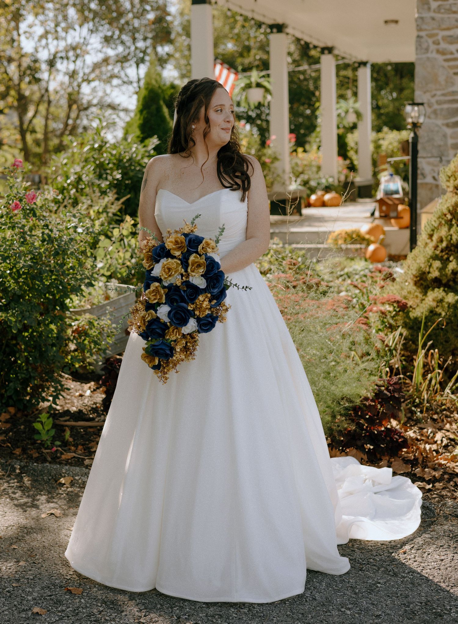 A wedding bouquet with navy blue and yellow flowers is held against a white ballgown dress in a garden setting.