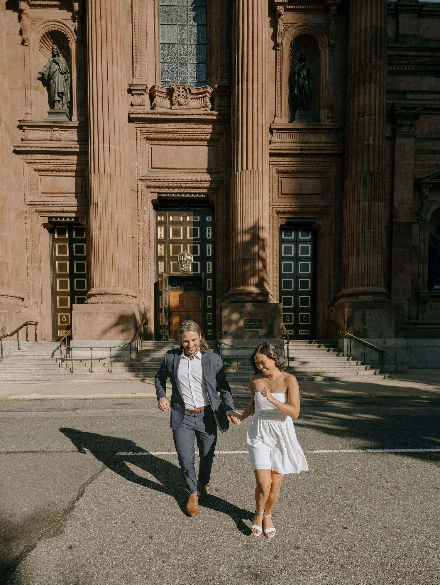 Couple walking and posing together in front of grand stone columns of a historic building.