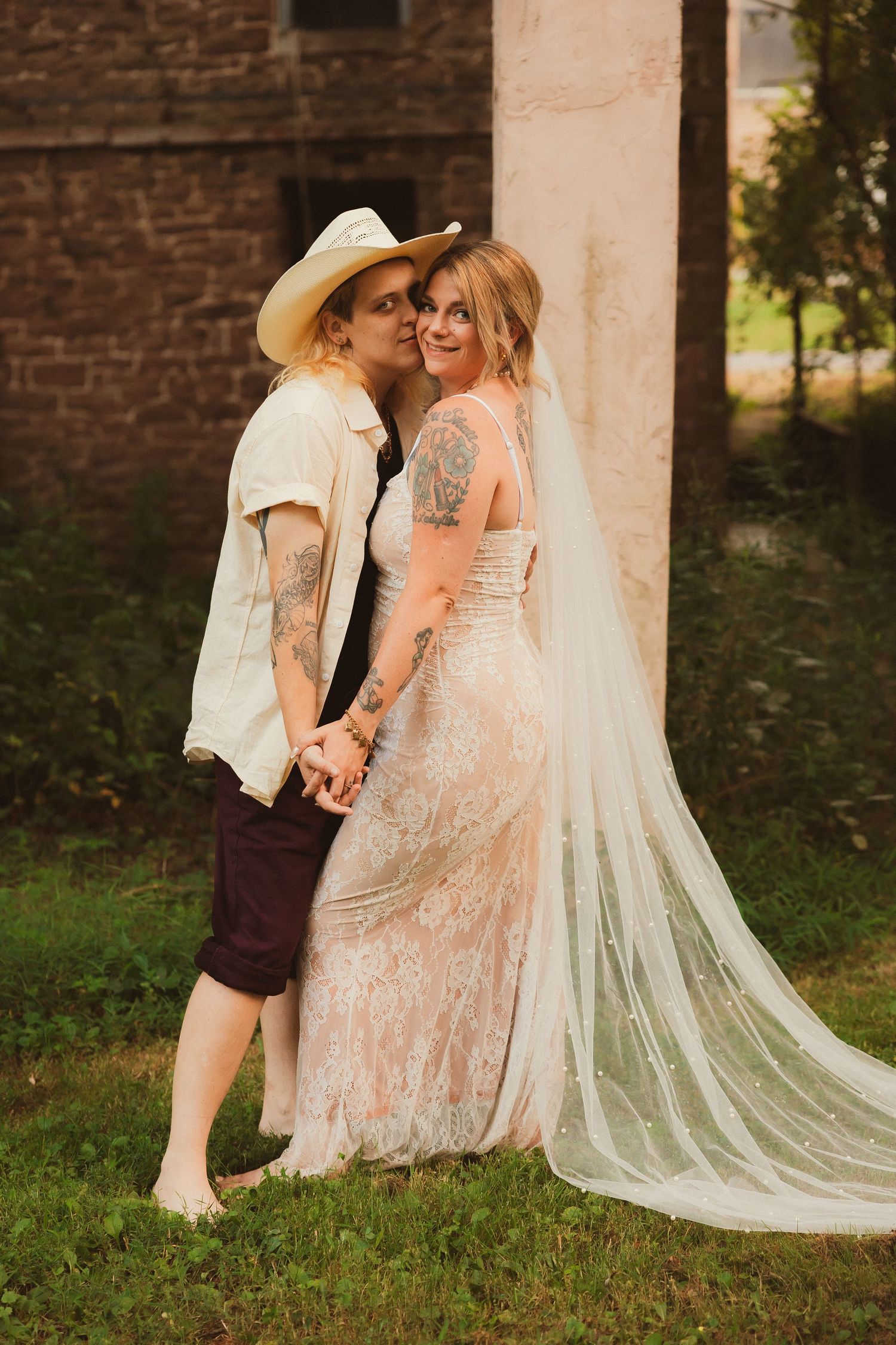 A wedding couple sharing a joyful moment against a brick wall backdrop.