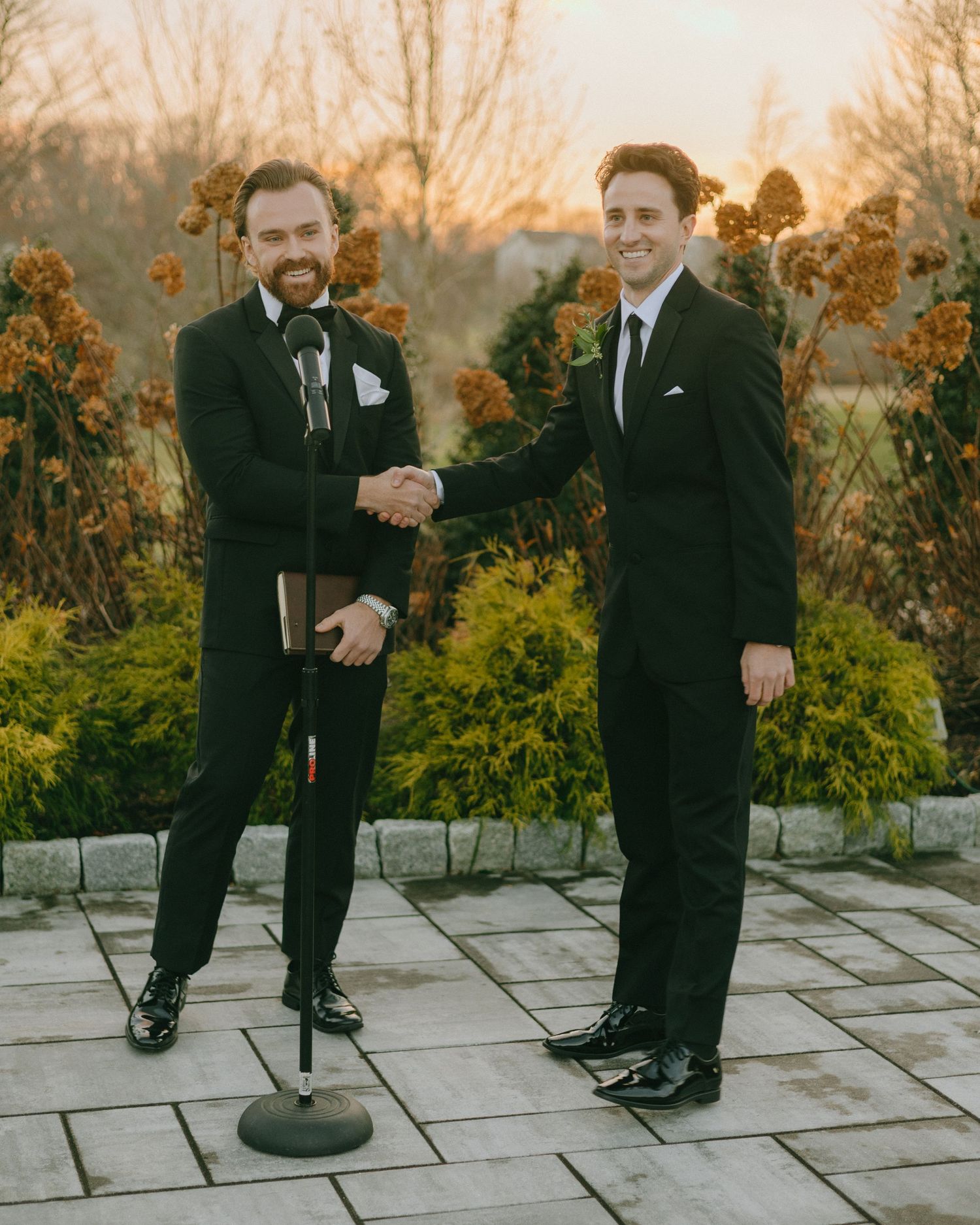 Two people in formal attire share a heartwarming moment on a stone patio during sunset.