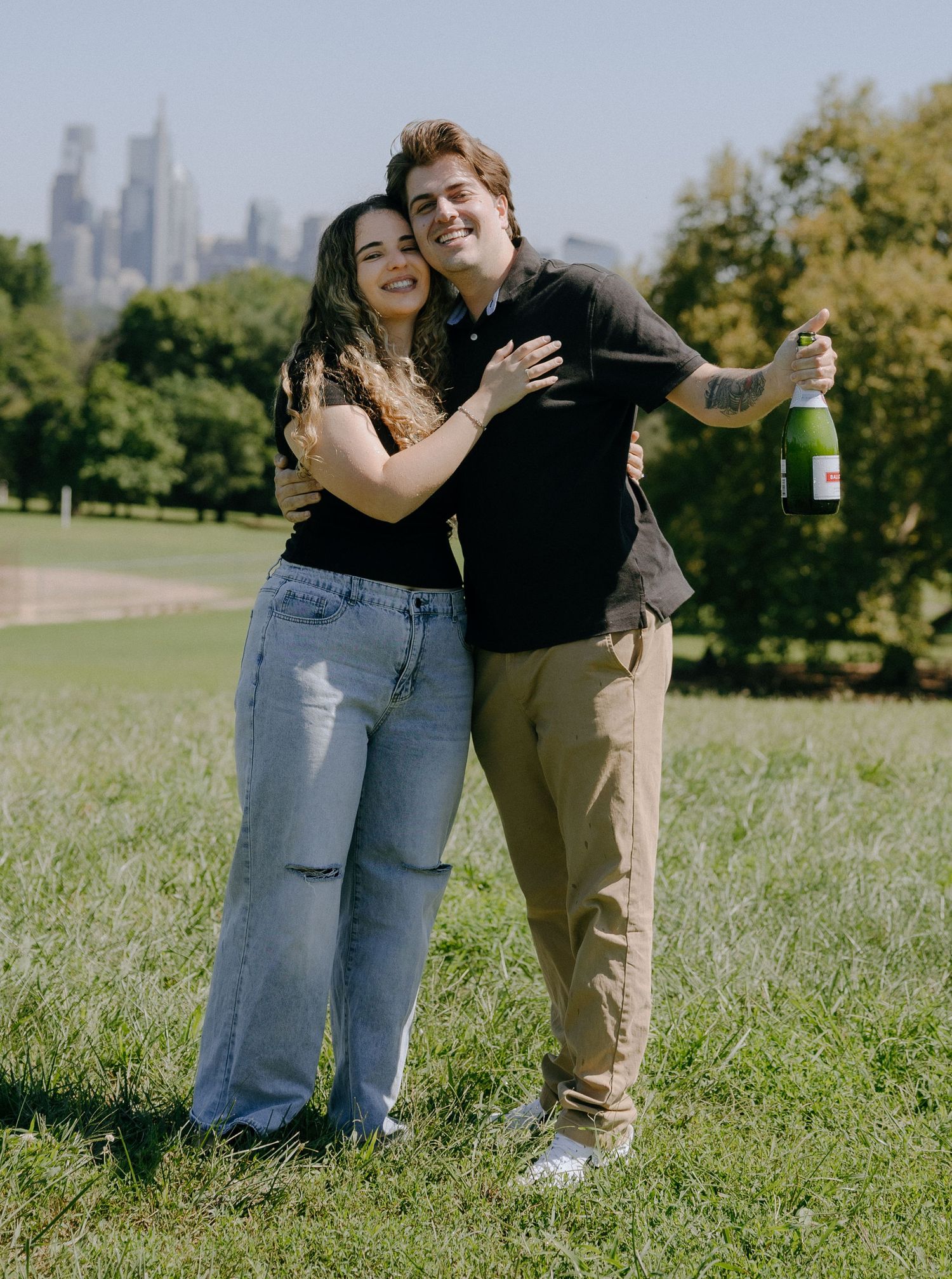 Two people share joyful laughter while celebrating with champagne in an urban park setting.