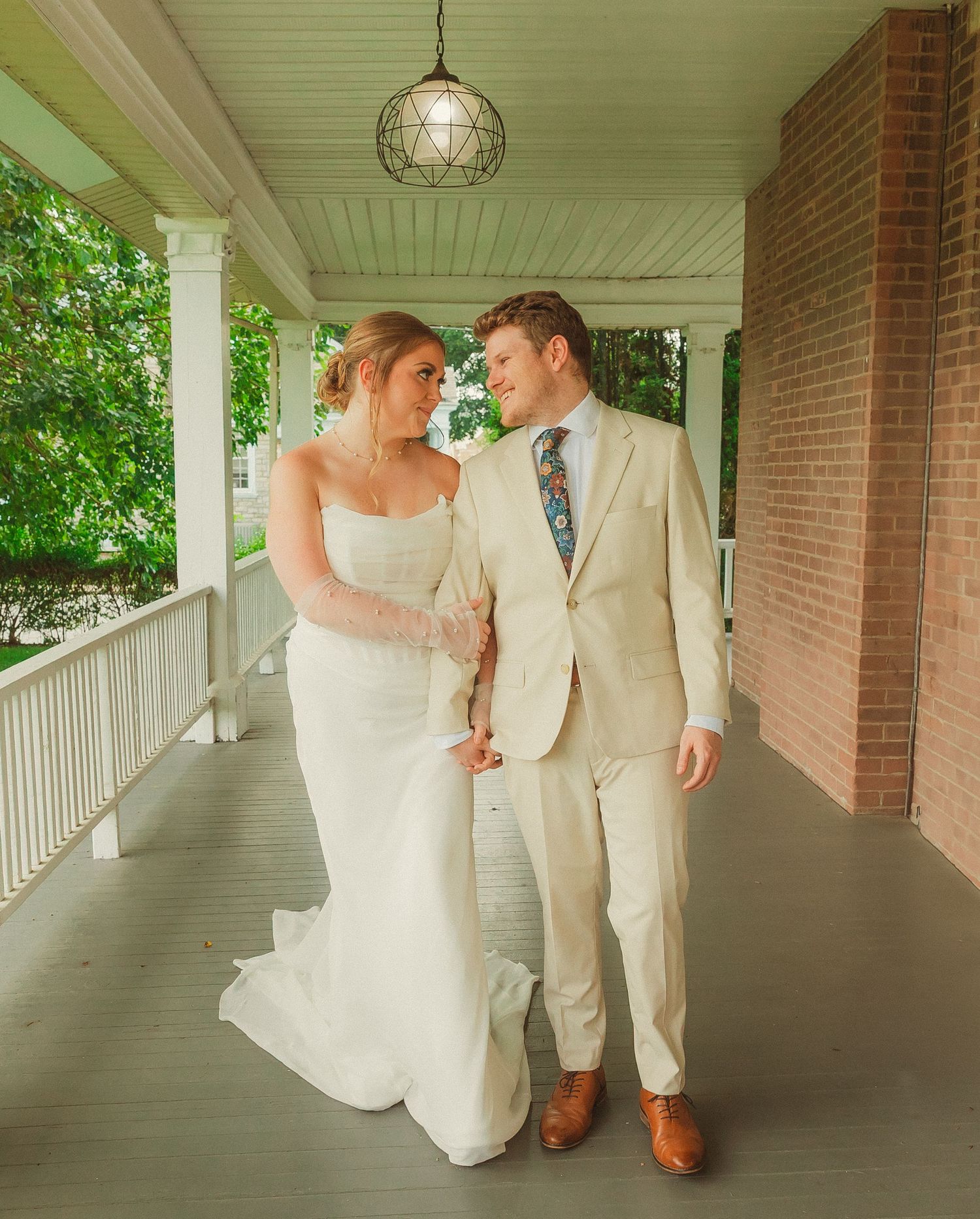 Couple in wedding attire walking together on classic southern style covered porch.