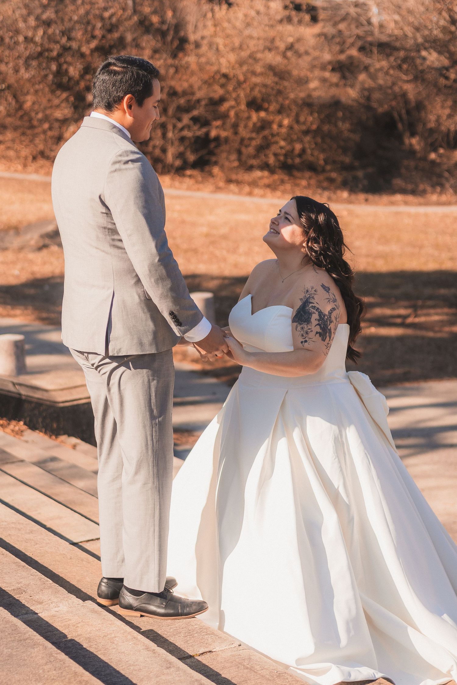 A couple sitting on steps outdoors, with the bride wearing a white wedding gown and groom in a light gray suit.