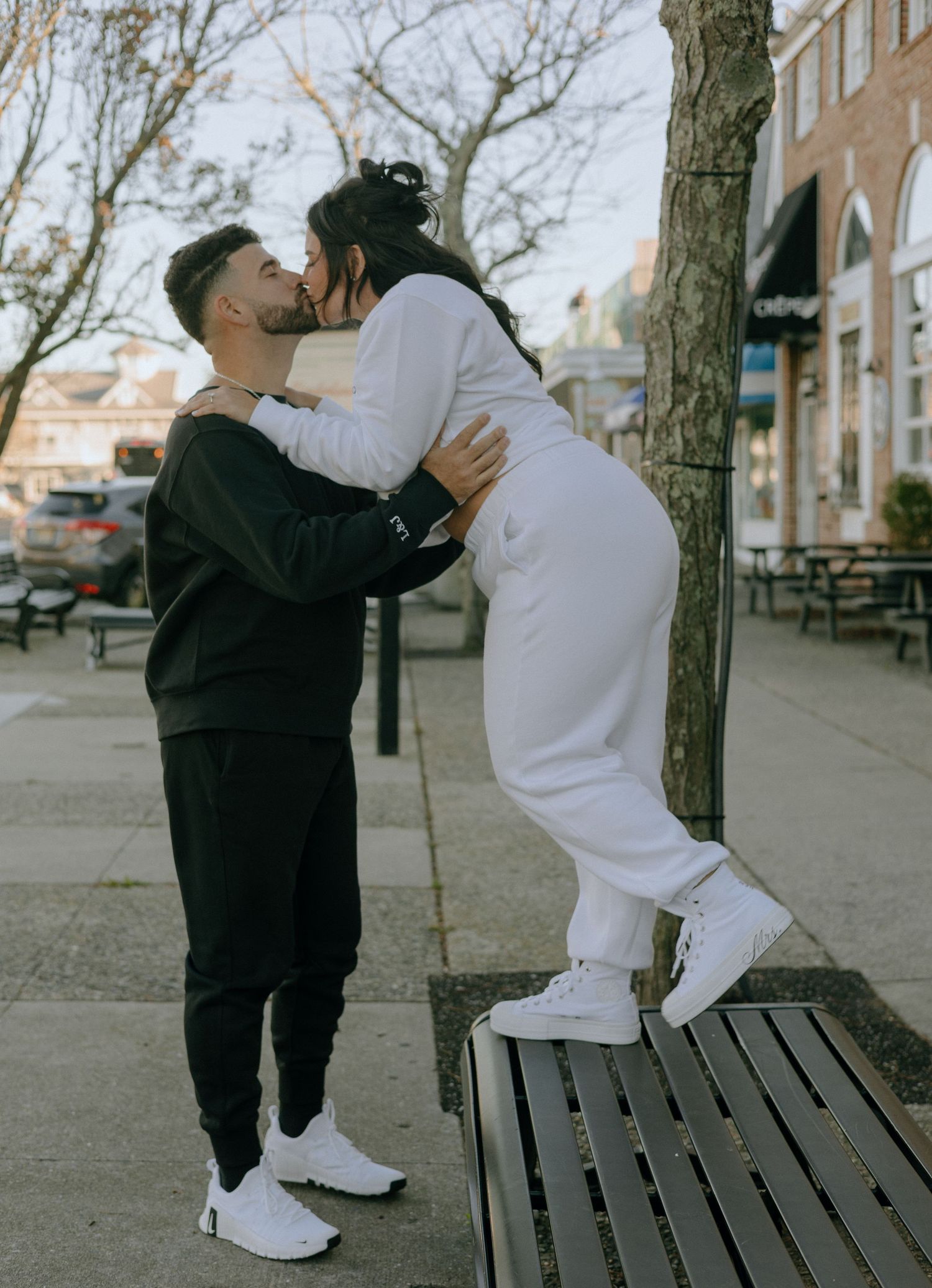 A sweet moment between a couple in matching white sneakers on an urban sidewalk.
