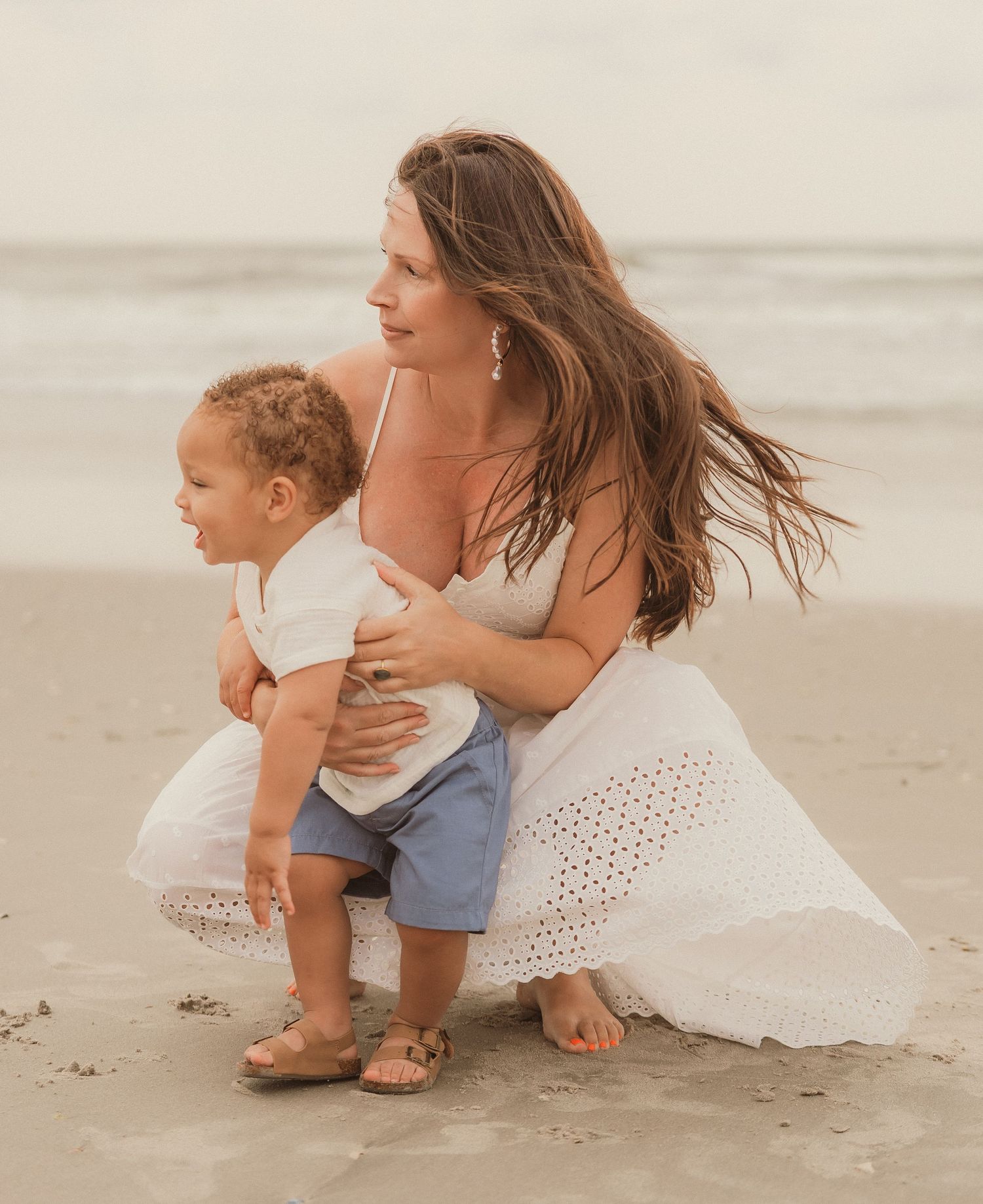 Mother and child share intimate moment on beach during family photoshoot.
