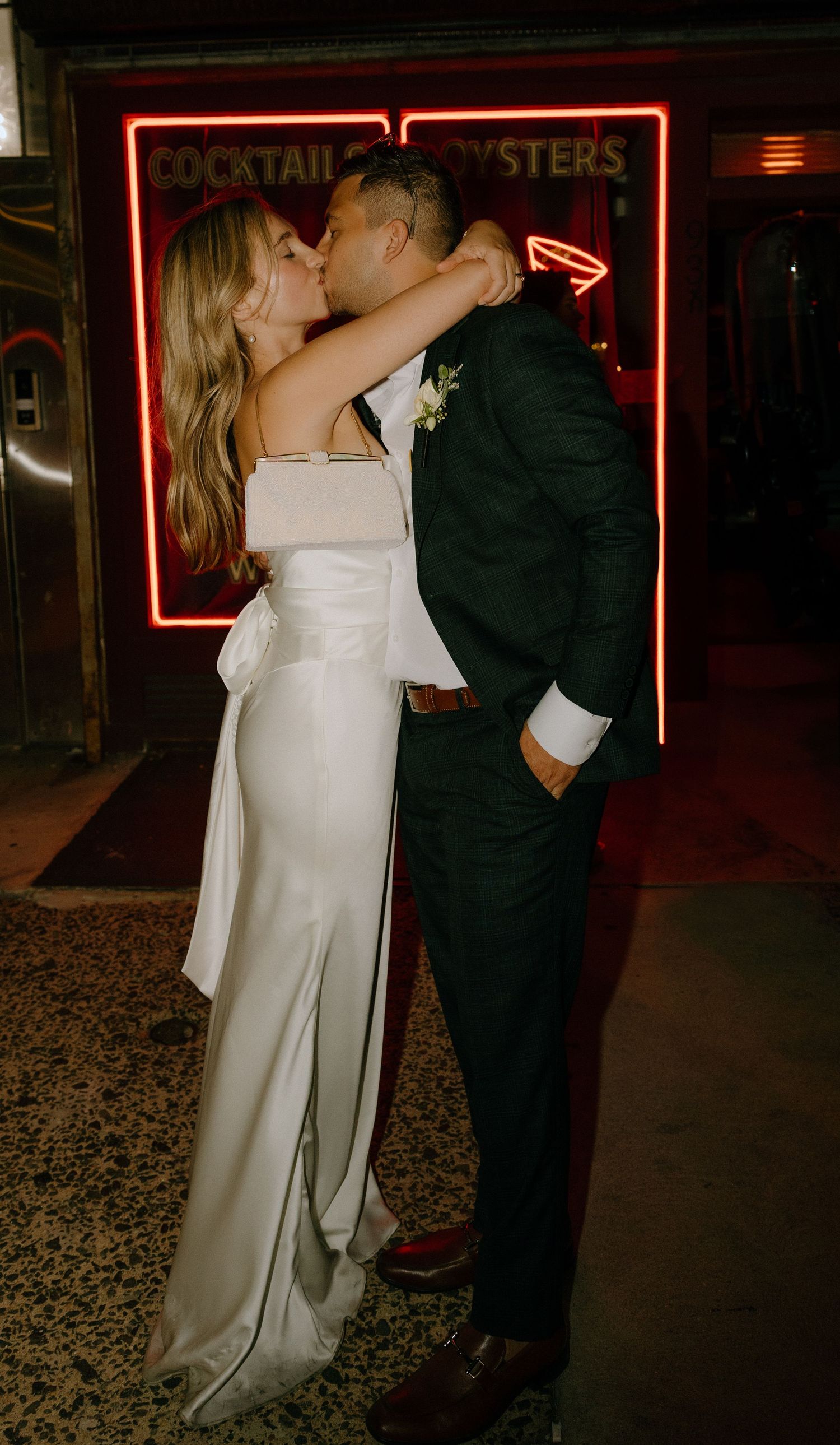 A romantic wedding moment captured under red neon lights in a vintage bar setting.