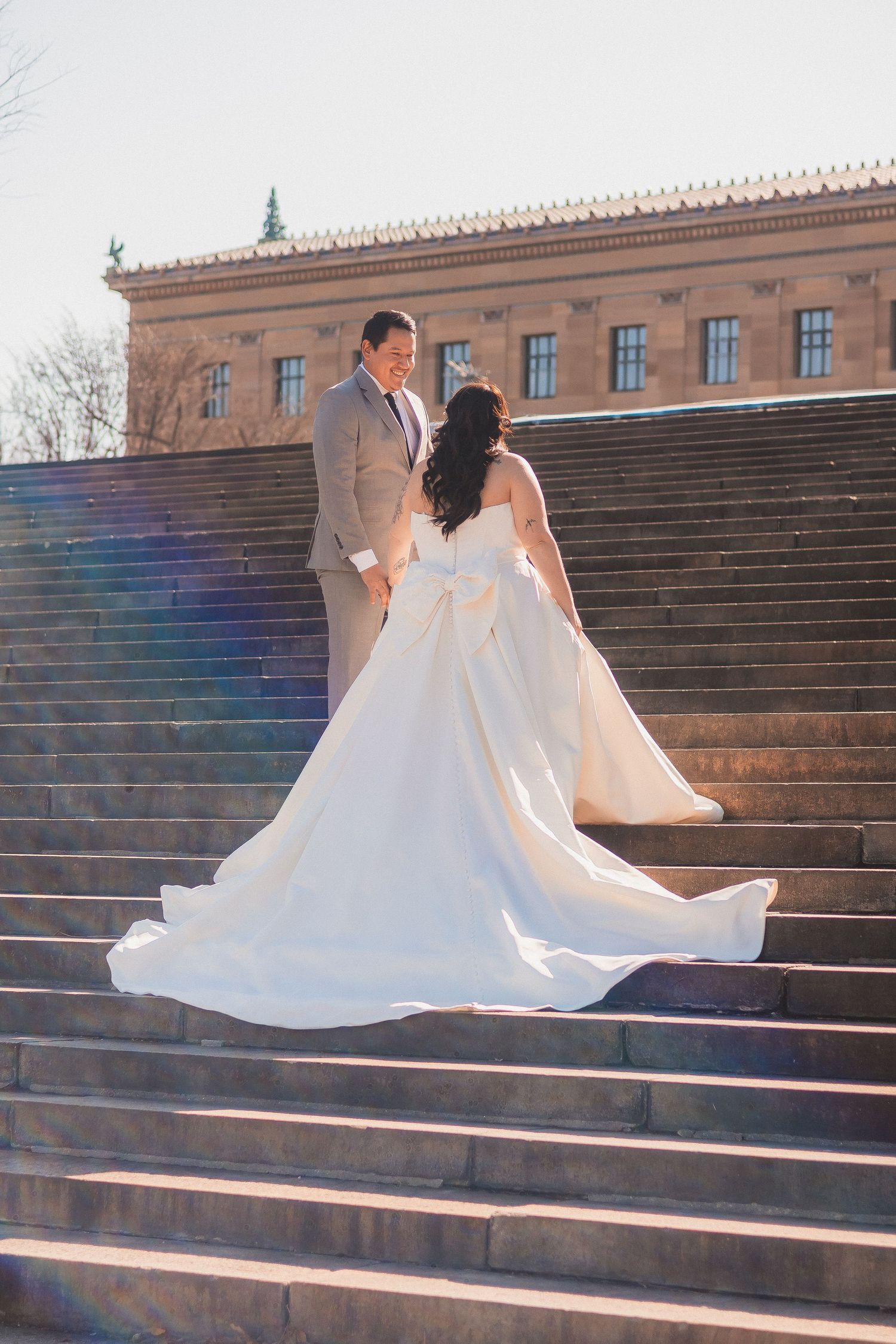 Wedding dress train flowing elegantly across stone steps against a classic building backdrop.