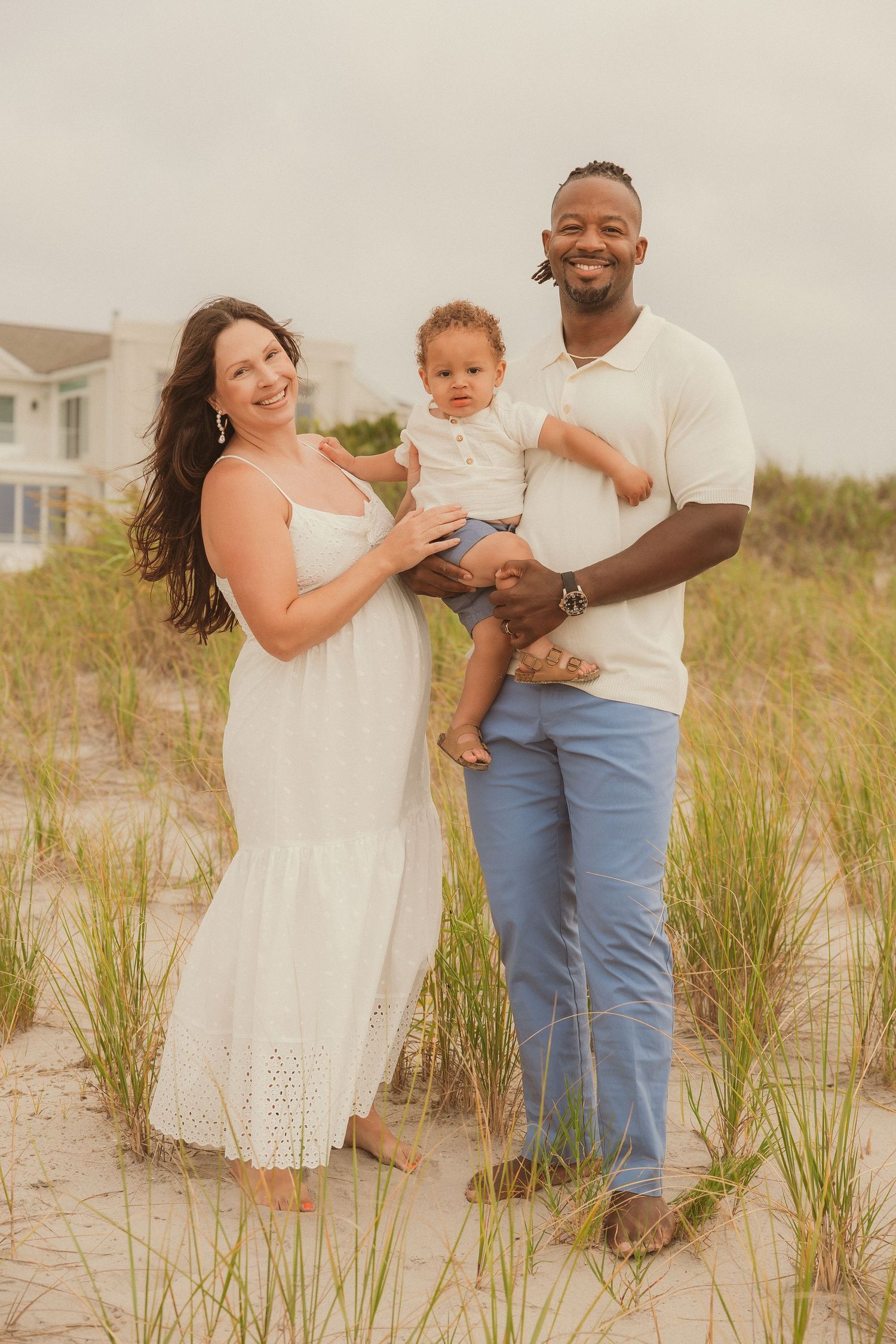 A family shares joyful moments among sand dunes and beach grass during a golden hour photoshoot.
