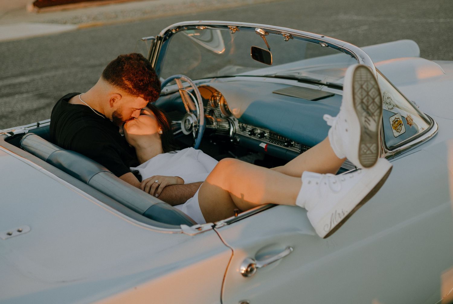 A person reclining in a vintage convertible car with a relaxed, laid-back posture on a sunny day.