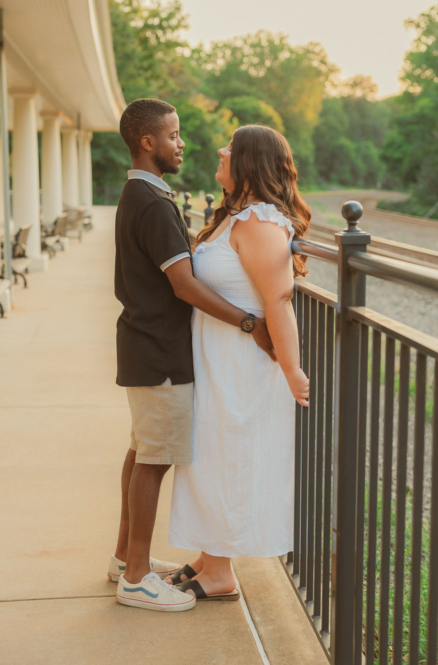 A couple embraces on a covered porch with white columns at sunset.