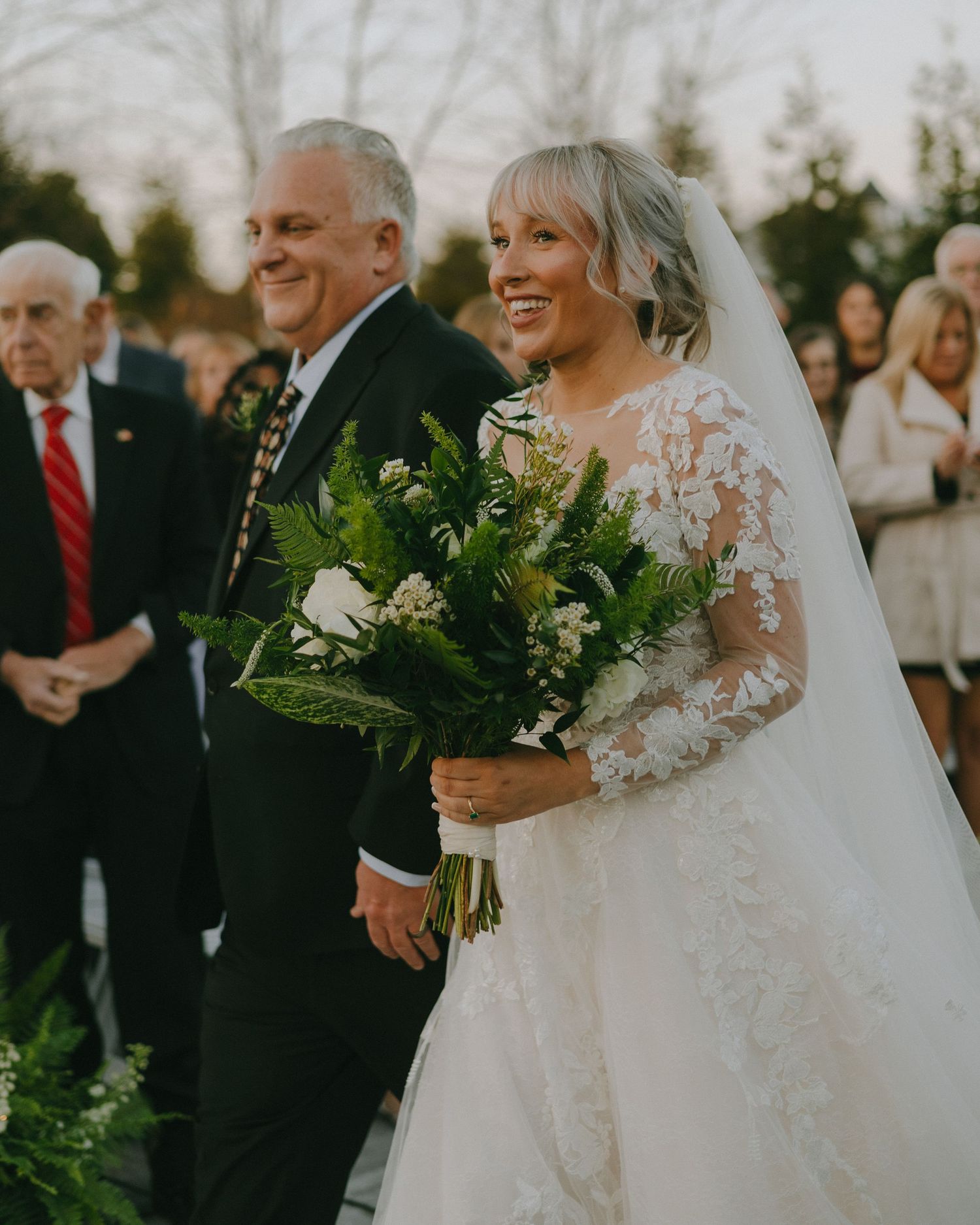 Joyful wedding party gathered outdoors during golden hour celebration with bride in elegant lace gown.