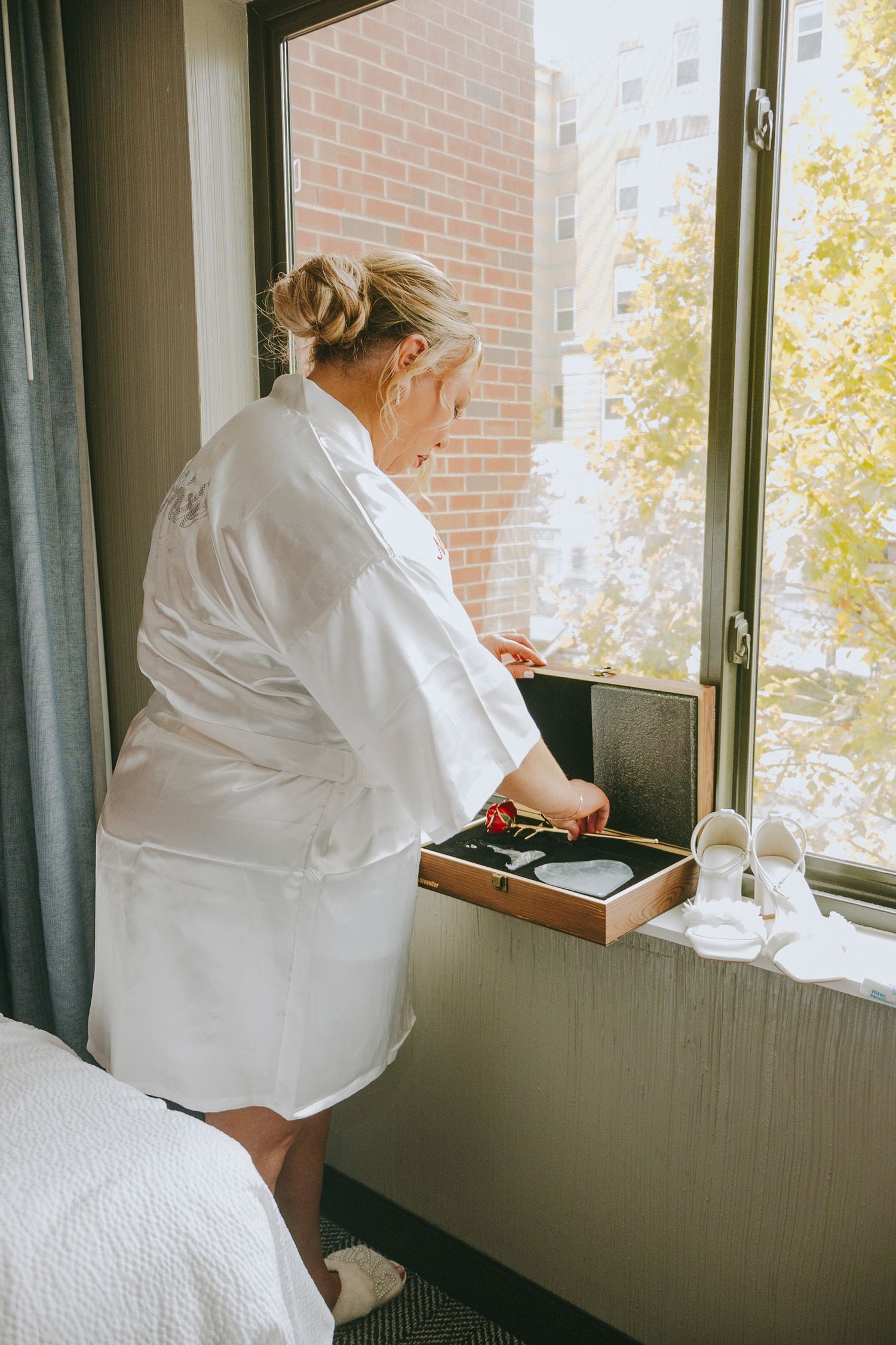 Person in white robe preparing morning coffee or tea by a sunny hotel window.