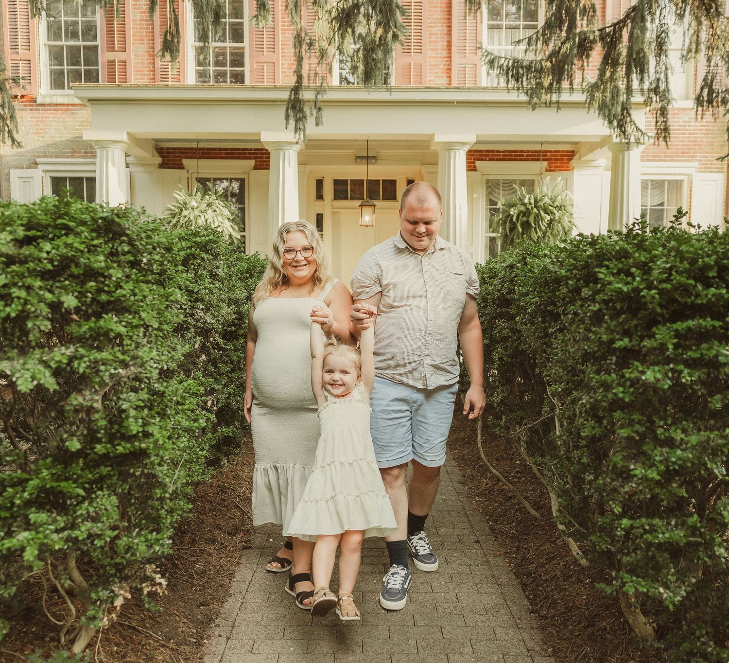 Family photoshoot outside classic colonial style house with landscaped garden.