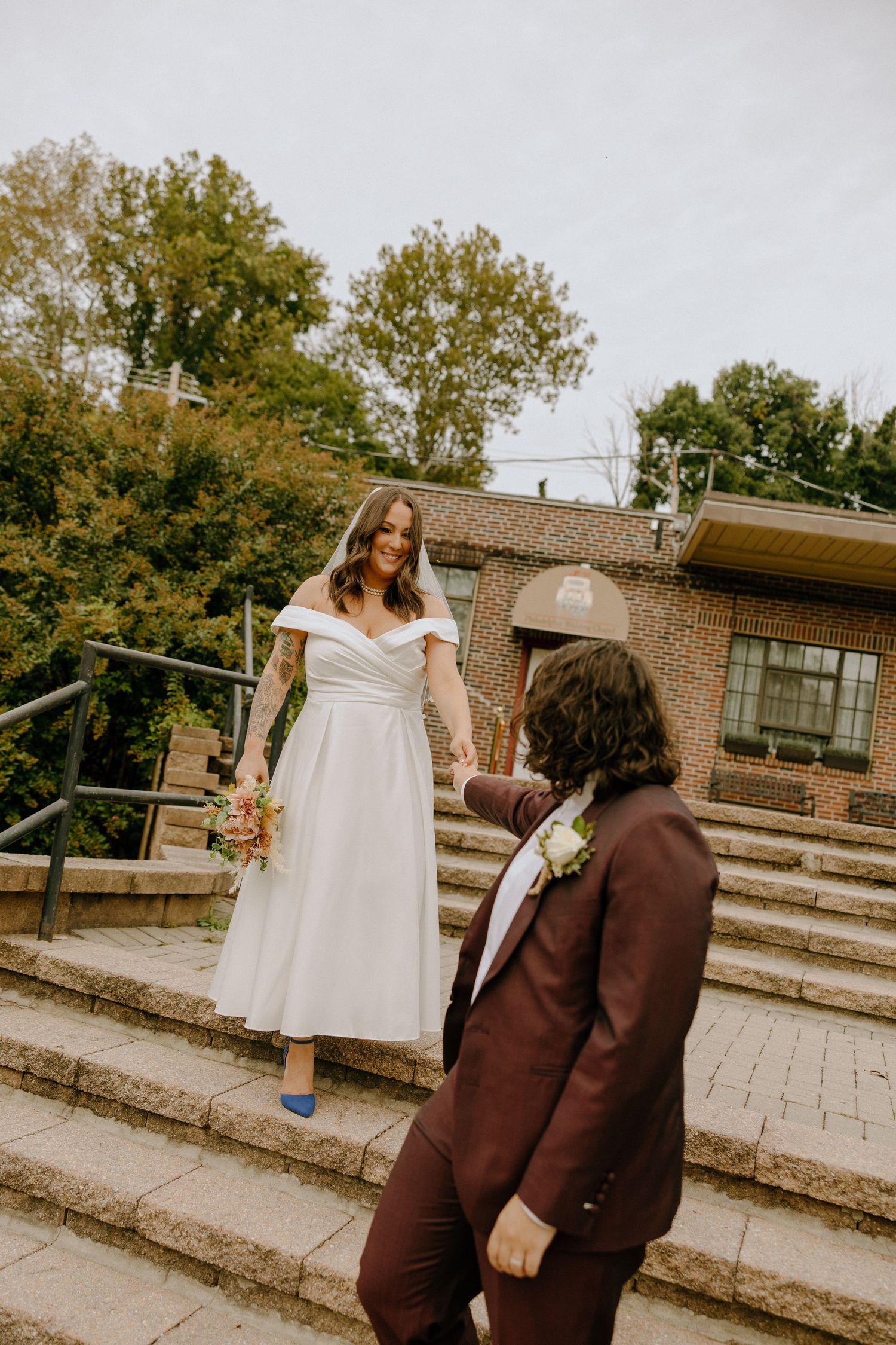 A couple stands on brick steps outside a chapel, with one wearing a brown suit and the other in white.