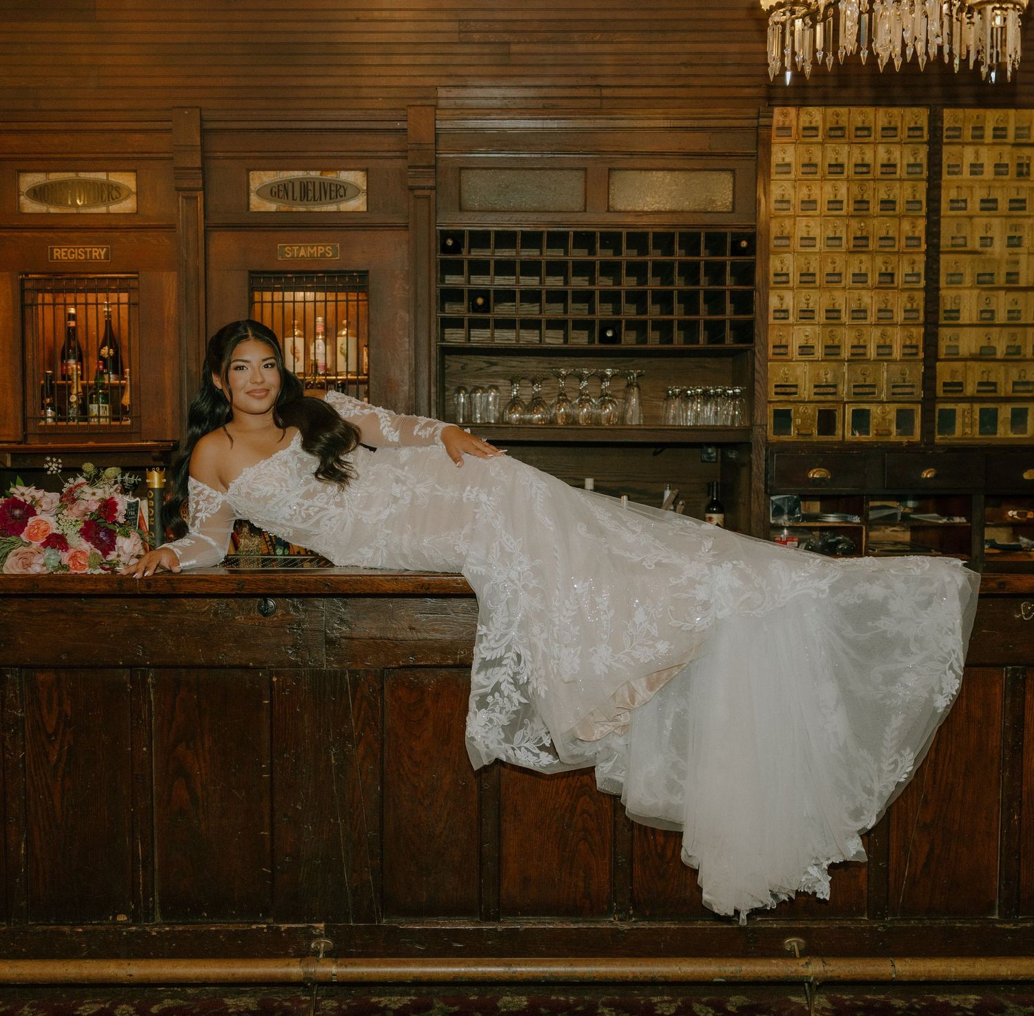 A wedding dress with lace details photographed in a vintage bar setting with wooden cabinets.