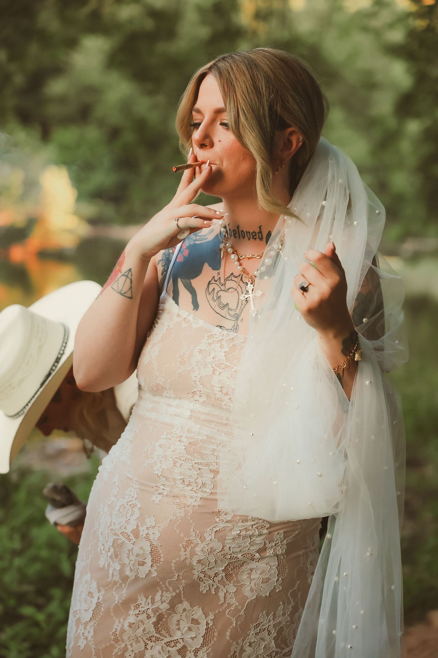 Bride in an elegant lace gown posing thoughtfully in a garden setting.