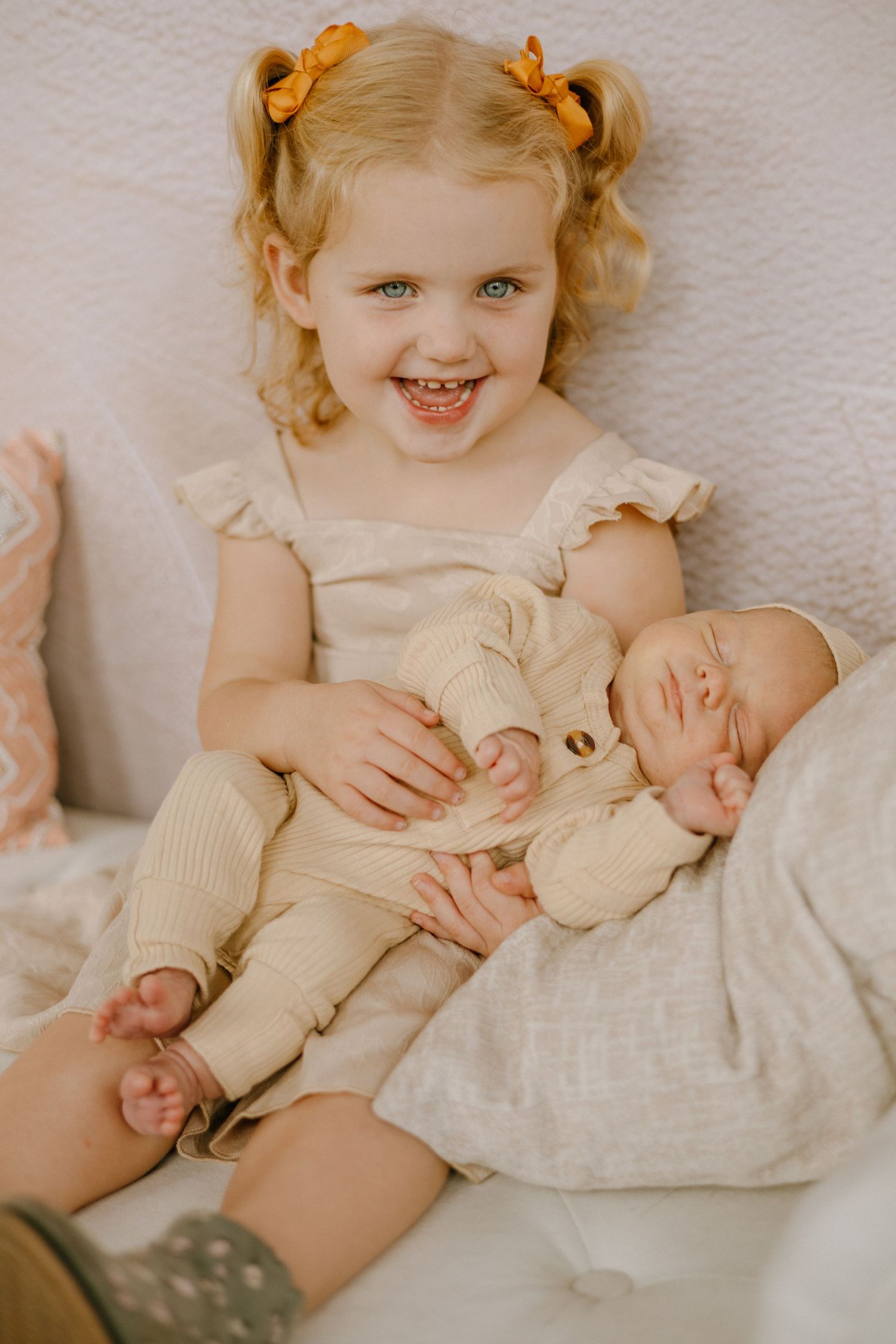 Sweet sibling portrait series showing tender moments between children on white bedding with yellow hair accessories.