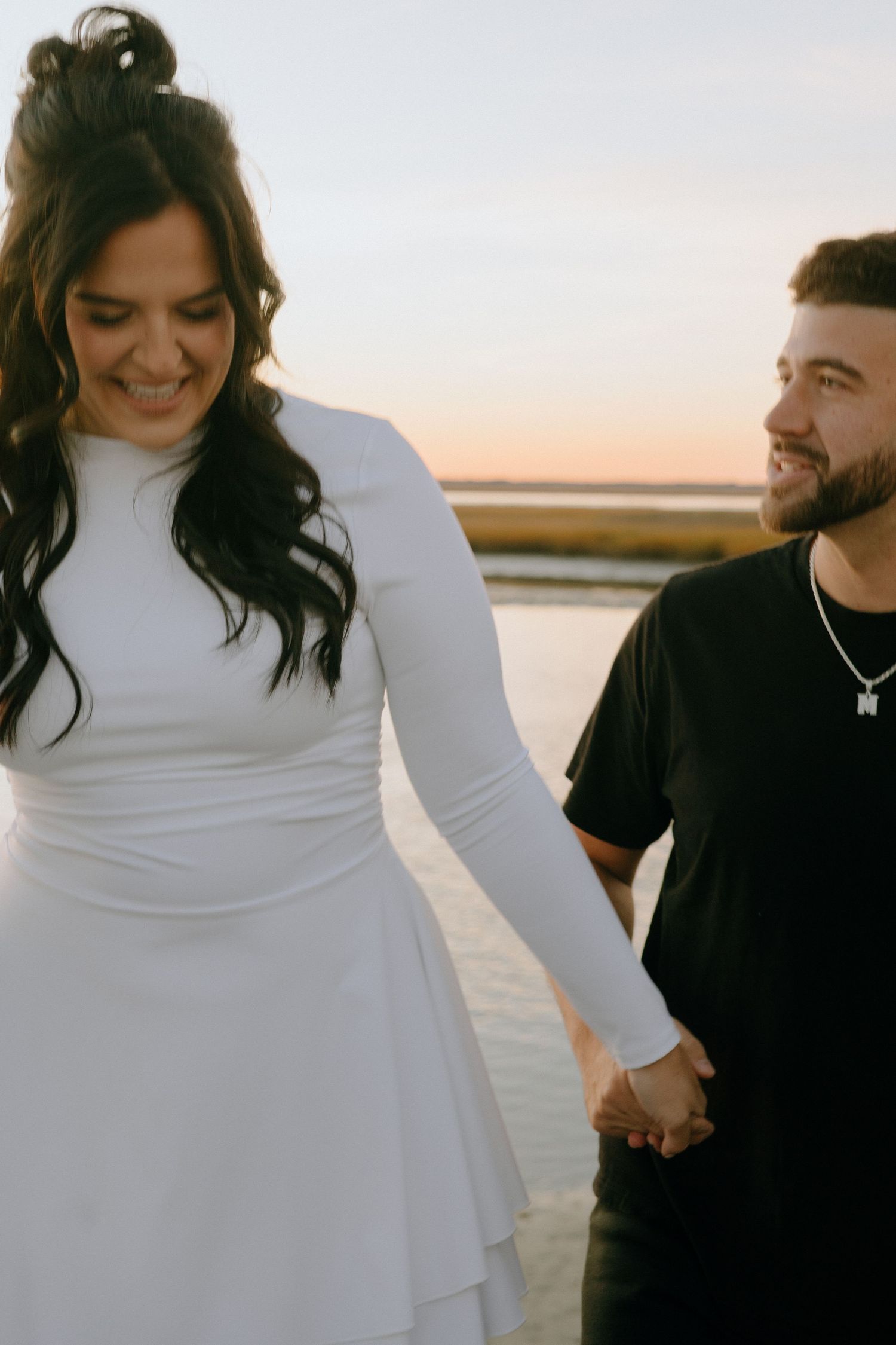 Couple in contrasting black and white outfits laughing together by the water during sunset.