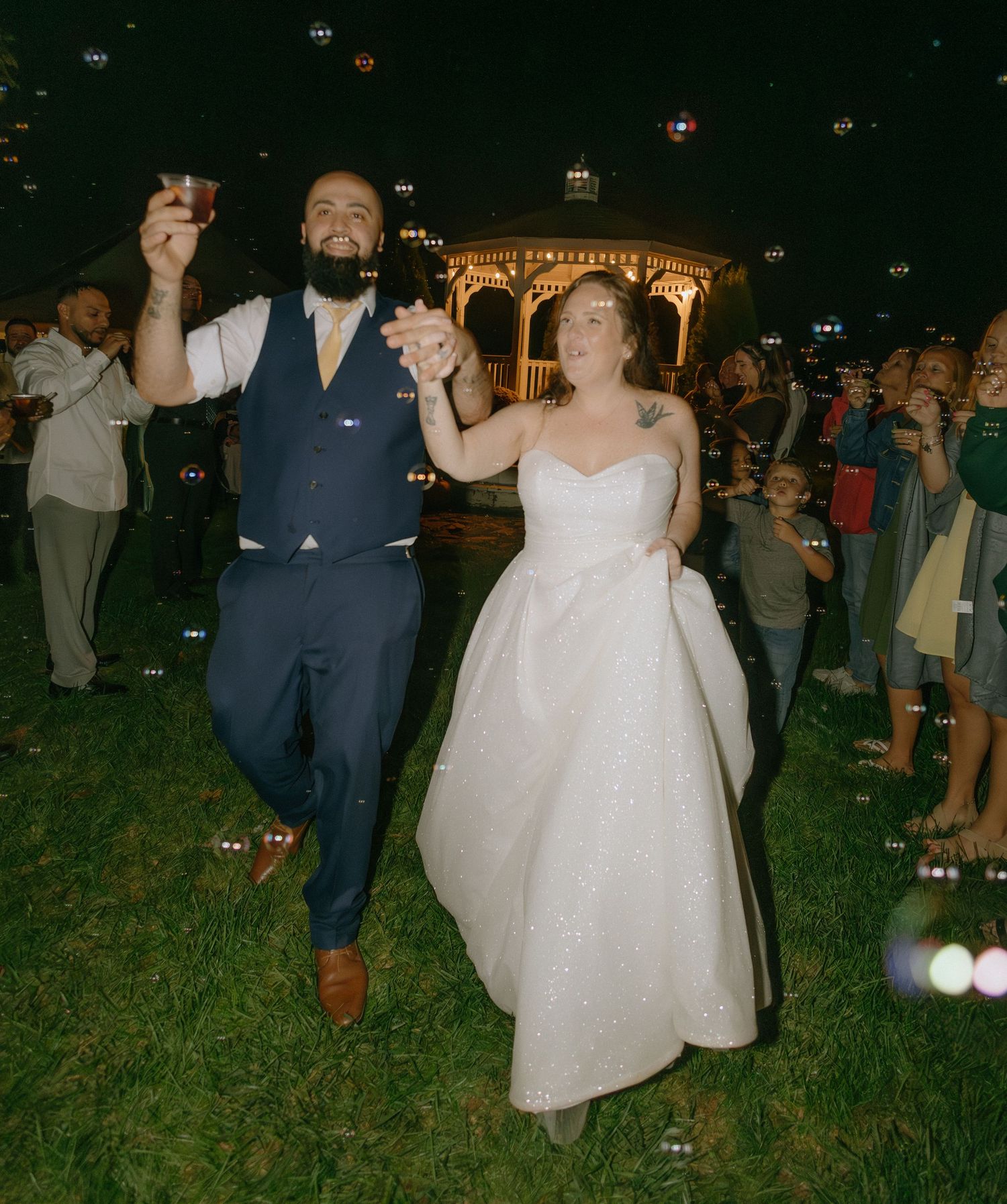 Wedding guests dancing outdoors at night under twinkling lights at a reception celebration.