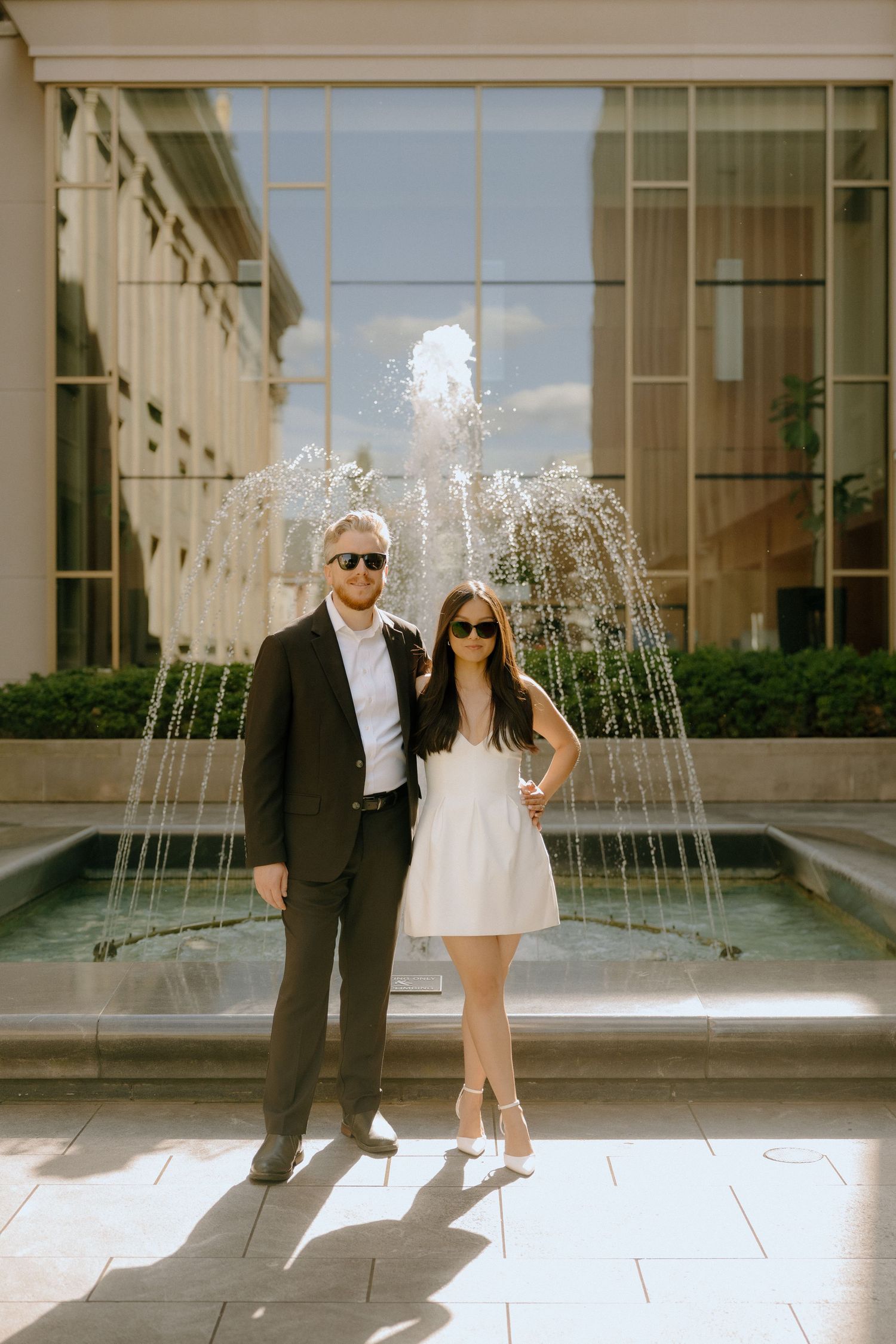 Couple in contrasting black and white outfits posing by an outdoor fountain.