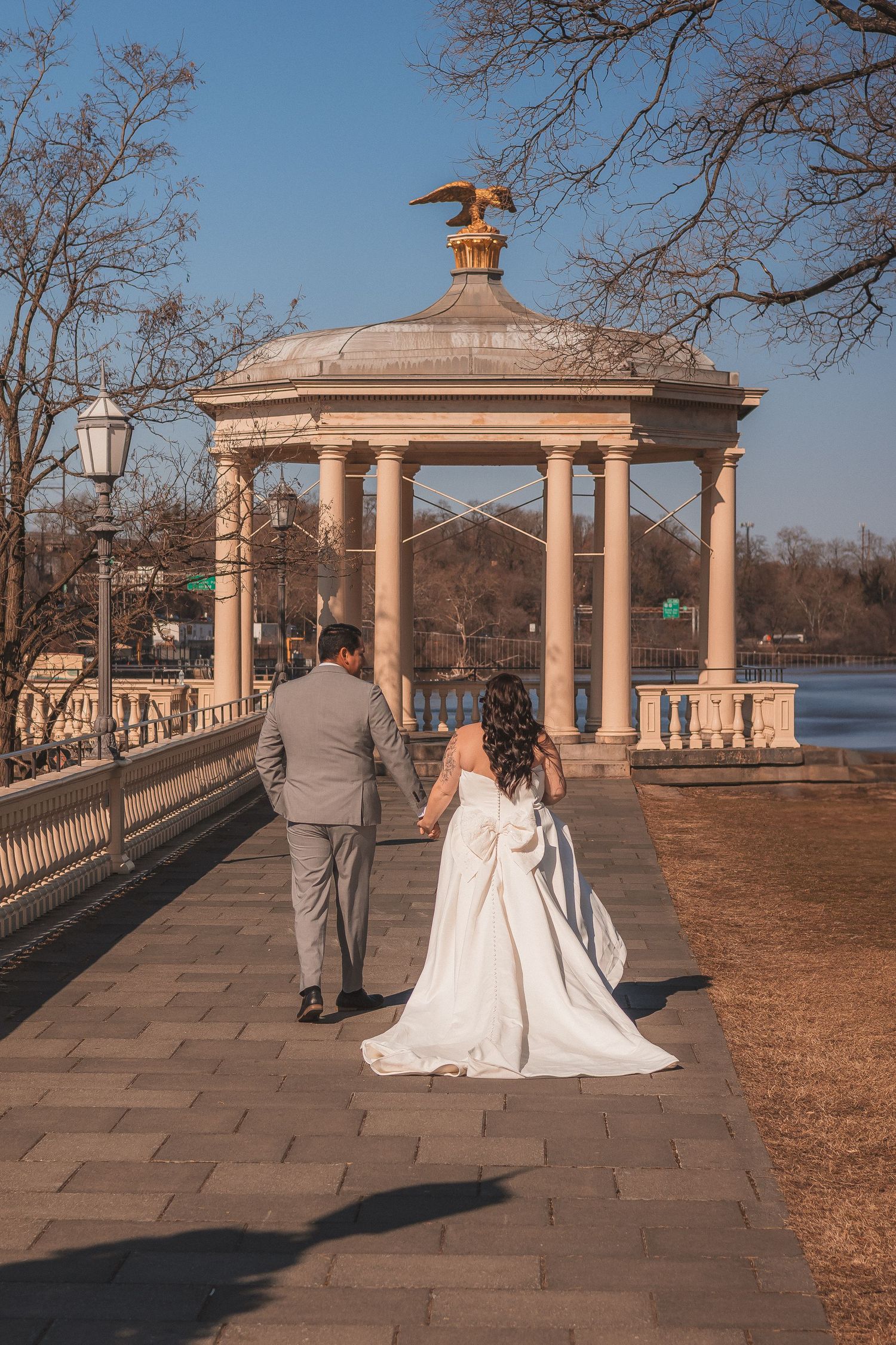Wedding couple walking along a waterfront promenade with classical gazebo and columns.