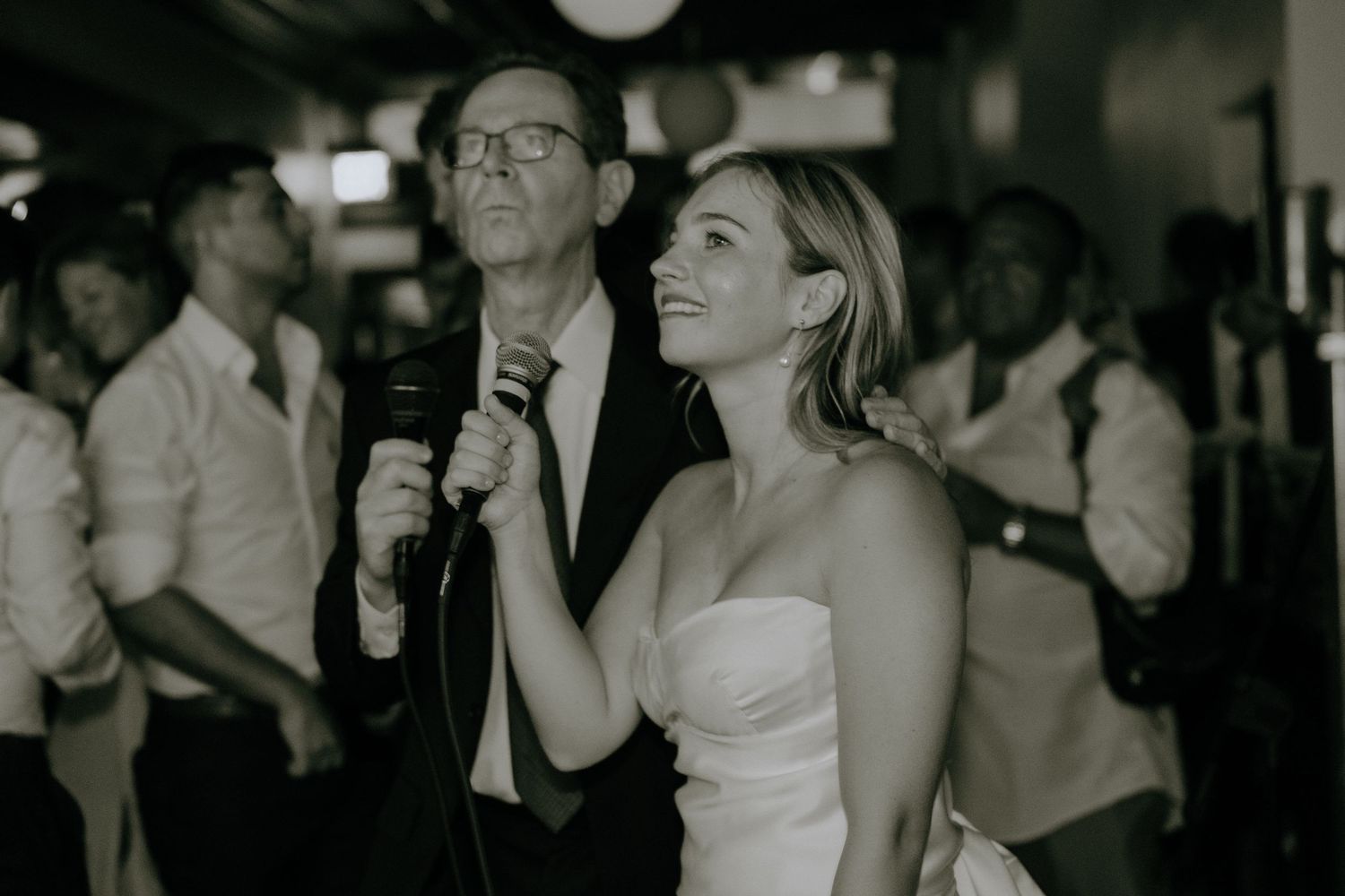 Wedding party members singing and celebrating during an indoor reception.