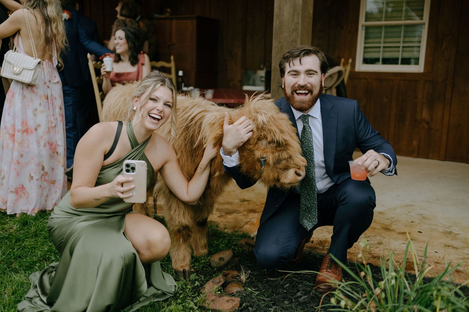 A group of wedding guests enjoying drinks and laughter at an outdoor rustic venue.