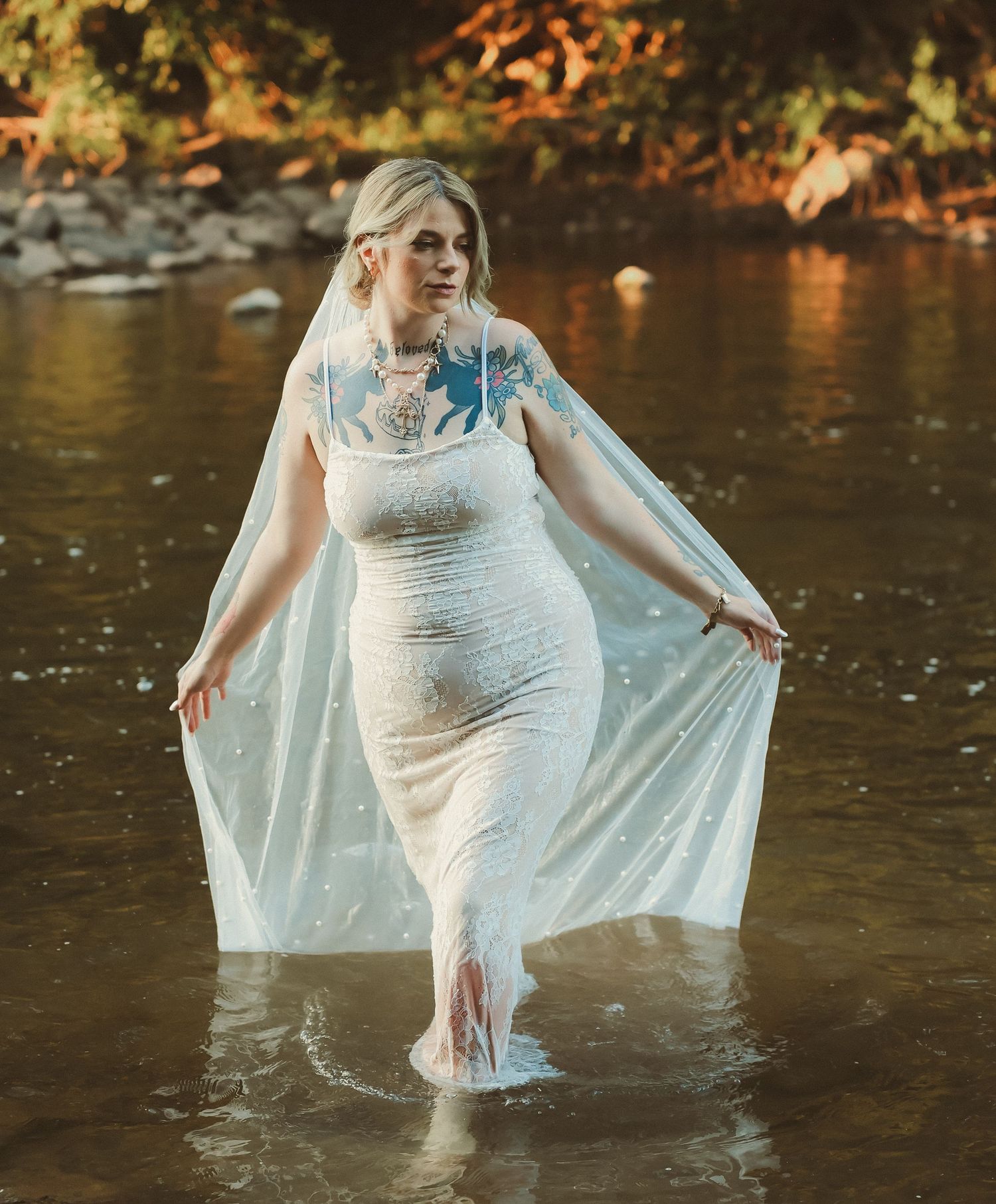 A person in a white wedding dress wading through water while holding up the long veil and skirt.