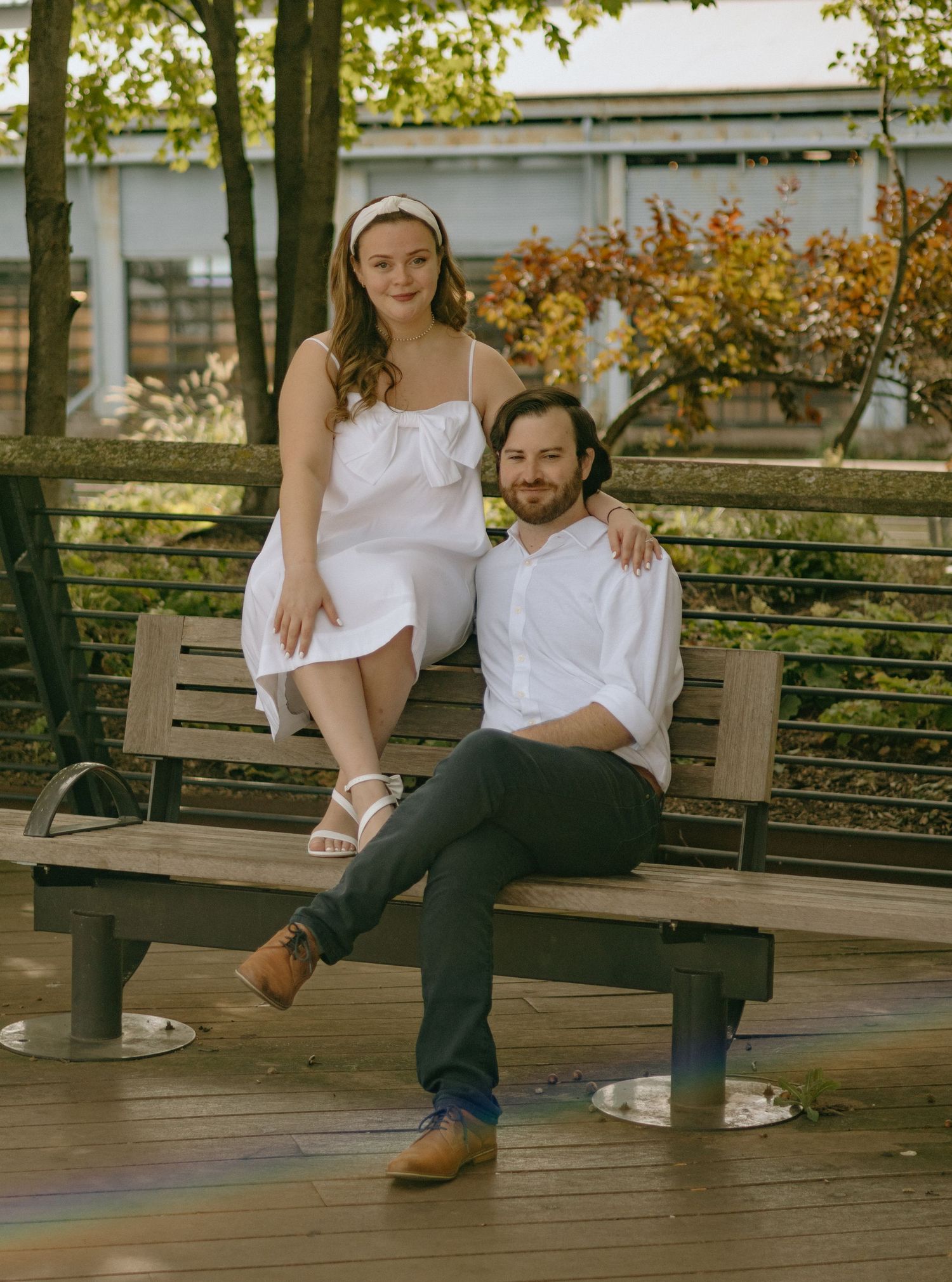 A couple relaxes and laughs together while sitting on a wooden bench in a park setting.