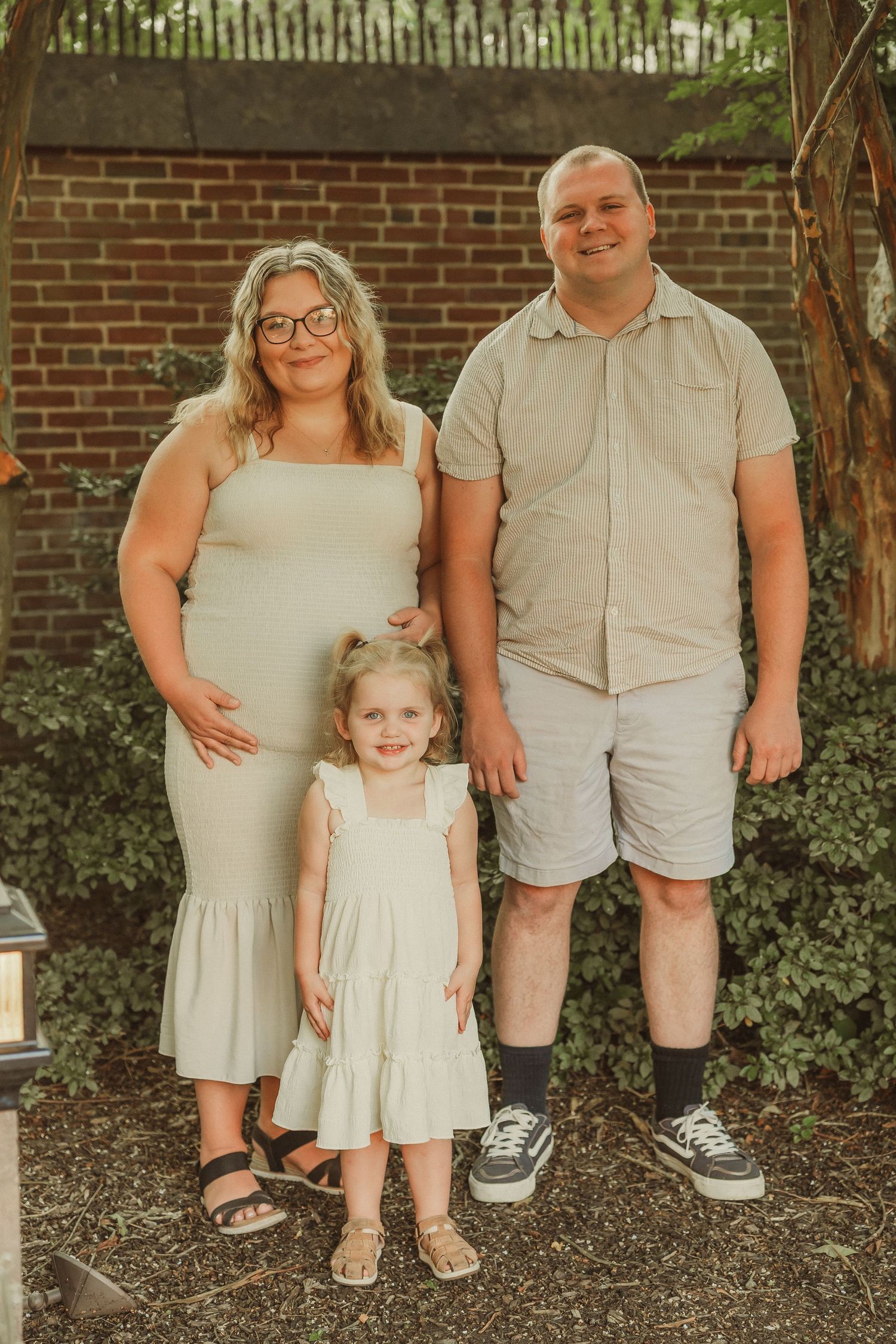 Casual family photo session showing coordinated neutral outfits against brick and foliage.