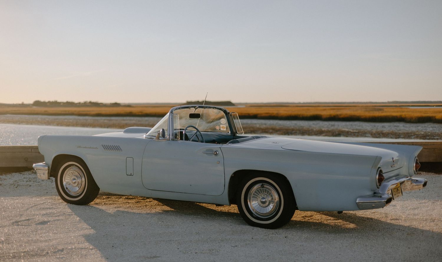 Classic vintage convertible car parked on a coastal road during sunset with ocean views.