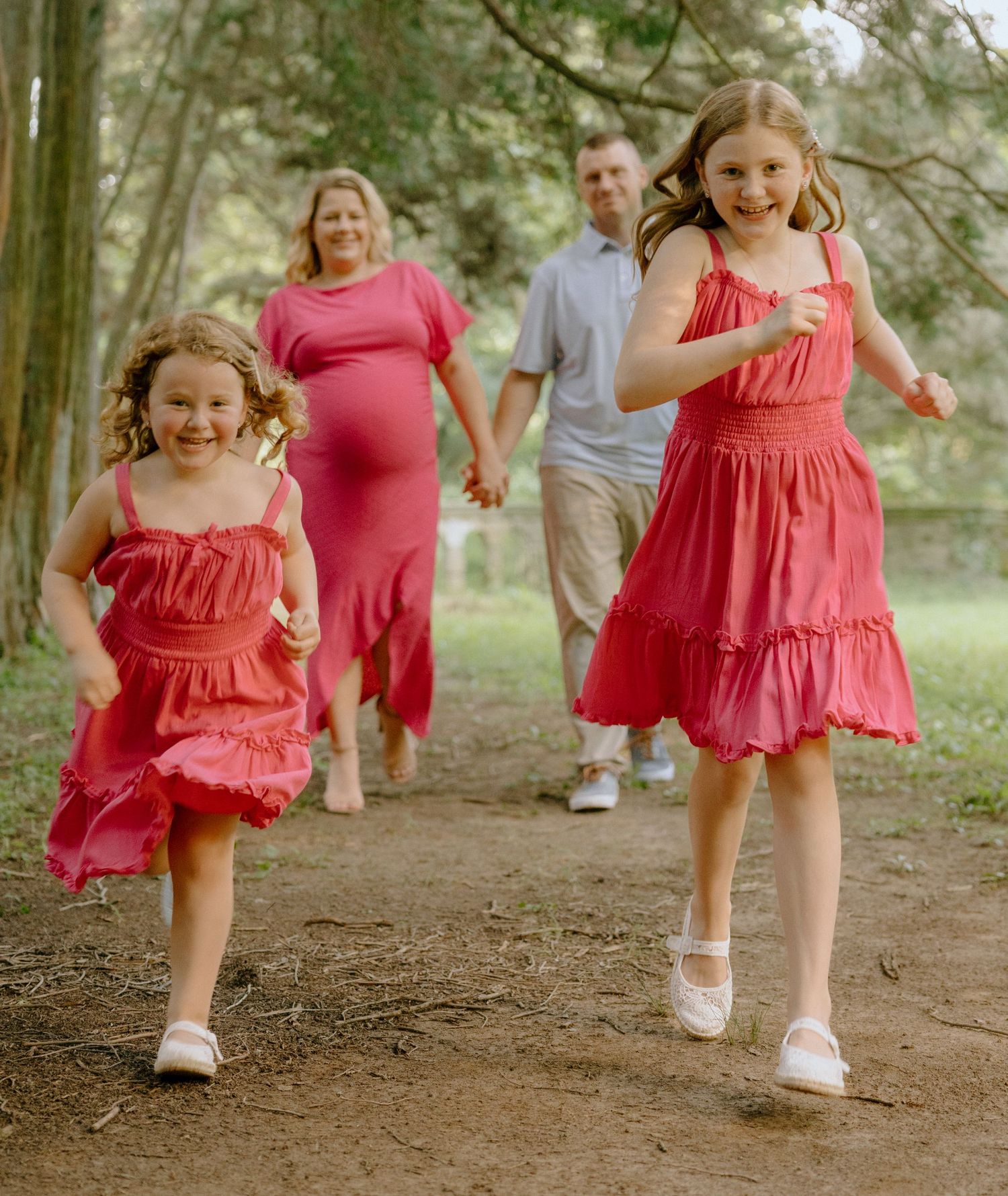 People in bright pink dresses walk along woodland path wearing white shoes.