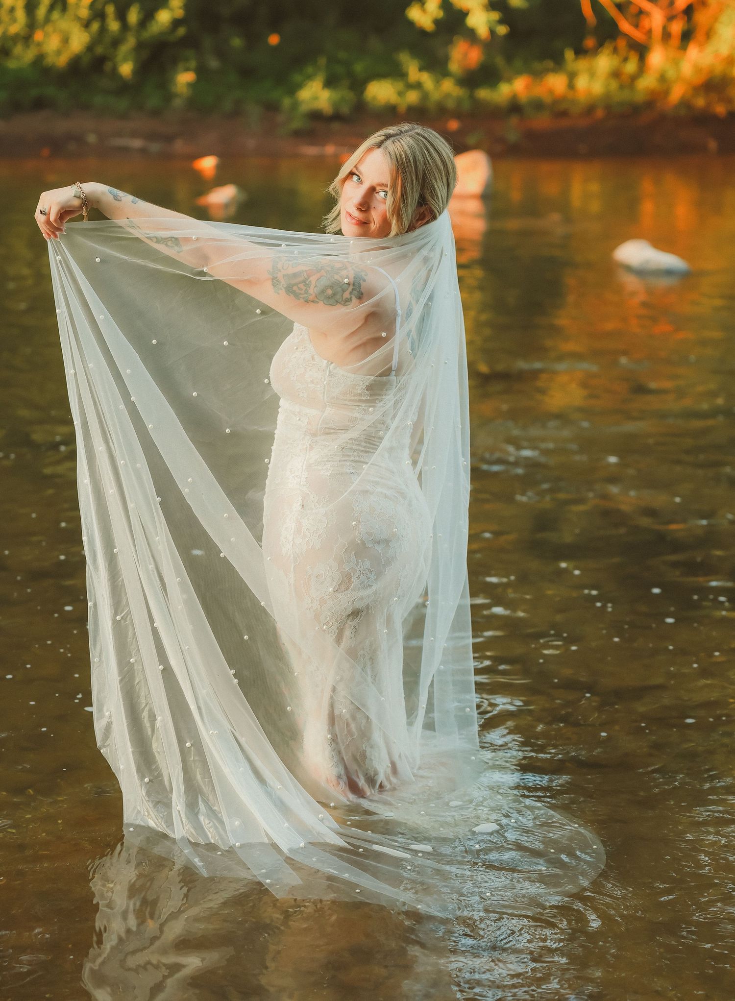 A wedding dress and veil flow elegantly in the rushing water of a scenic river.