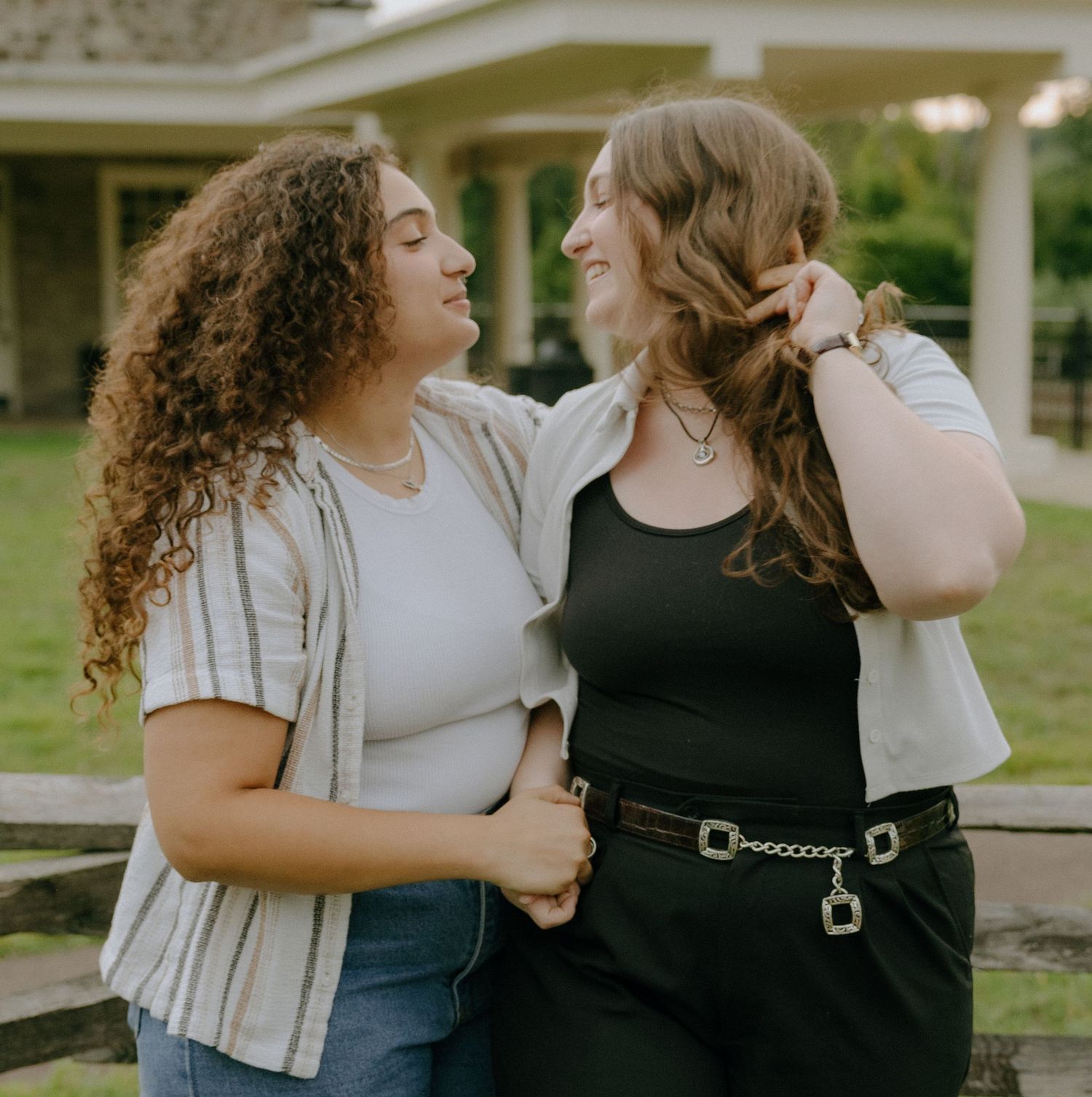 Two friends in casual outfits embrace and laugh together outdoors on a sunny day.