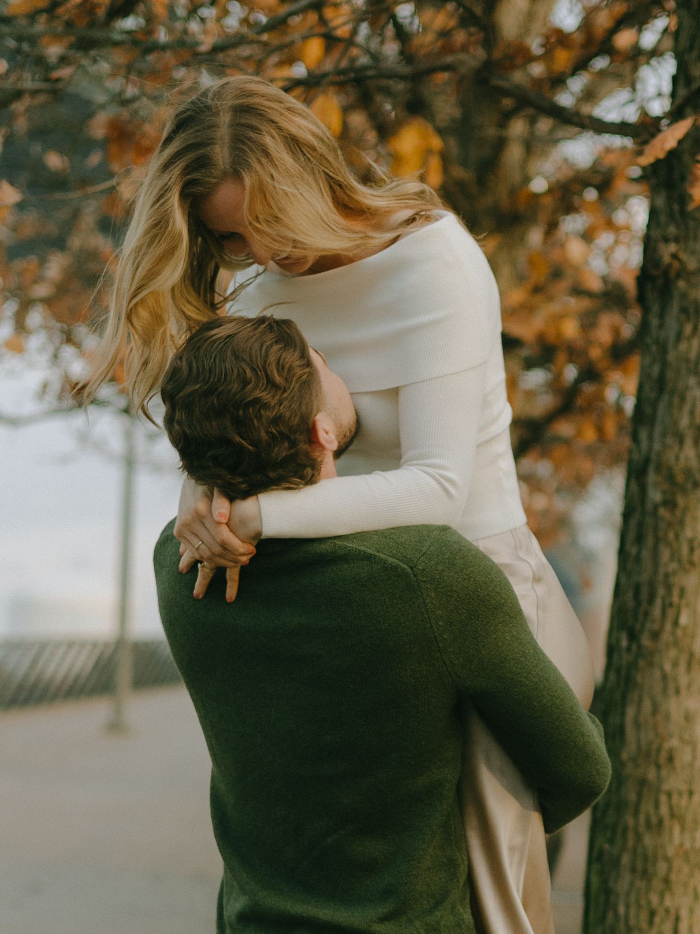 A couple embraces tenderly in an autumn forest setting with golden leaves in the background.