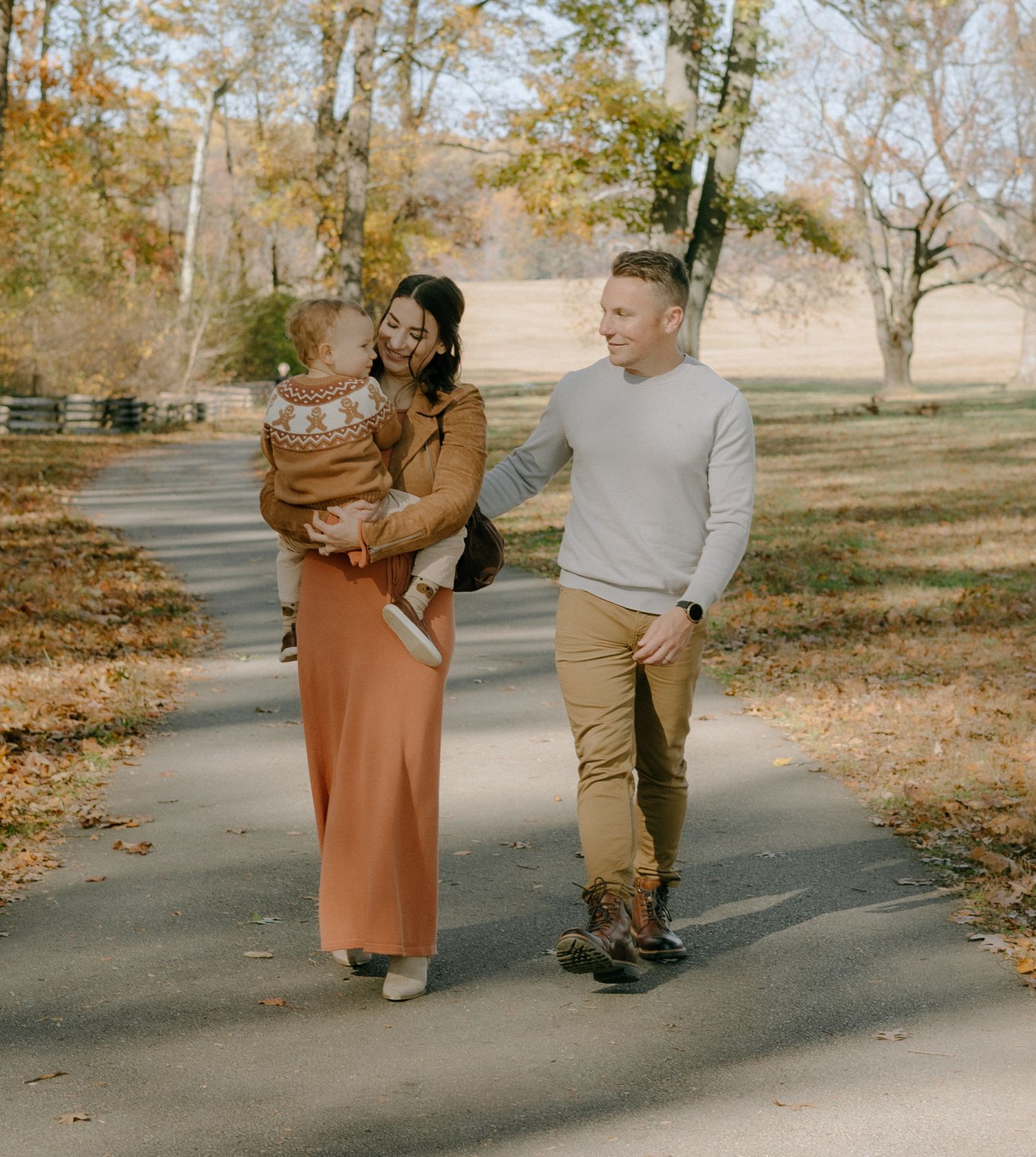 A couple walking together on a paved path surrounded by autumn trees and fallen leaves in a park setting.