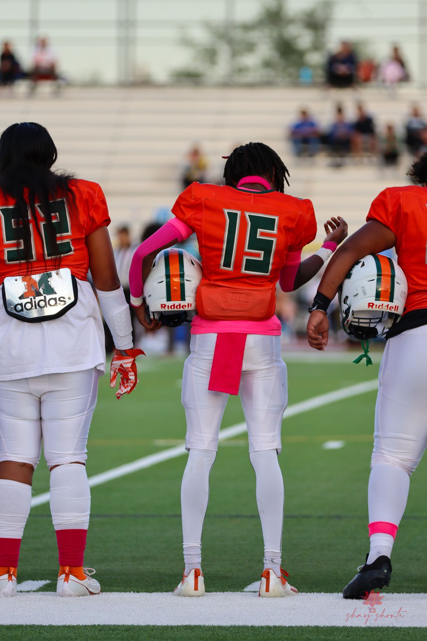 Football players in orange and white uniforms standing on sideline wearing jersey numbers.