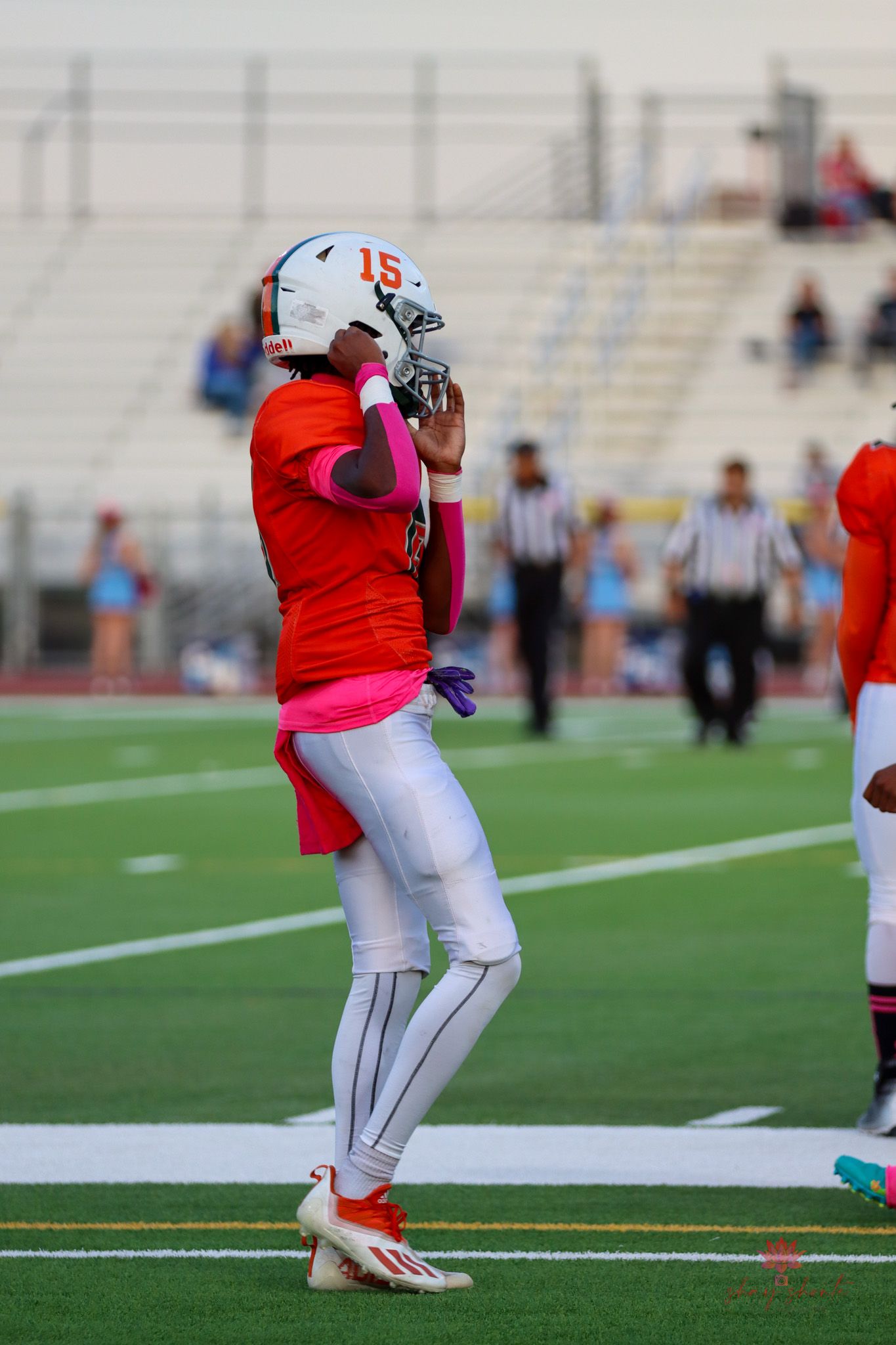 Player in orange uniform and white helmet stands ready on football field.
