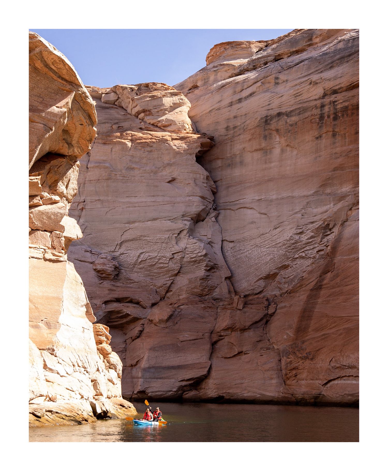 Small kayak dwarfed by massive sandstone cliffs in a narrow water-filled canyon.