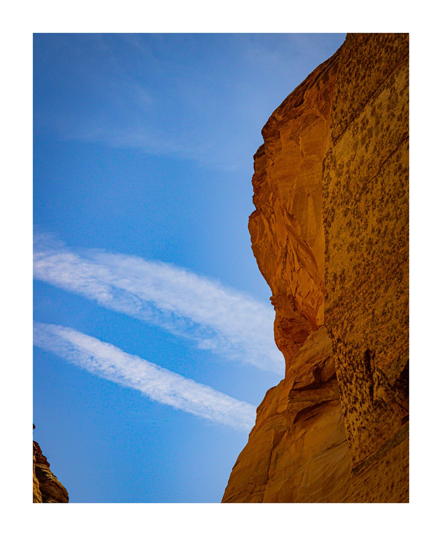 Towering sandstone cliff face against bright blue sky with wispy clouds.