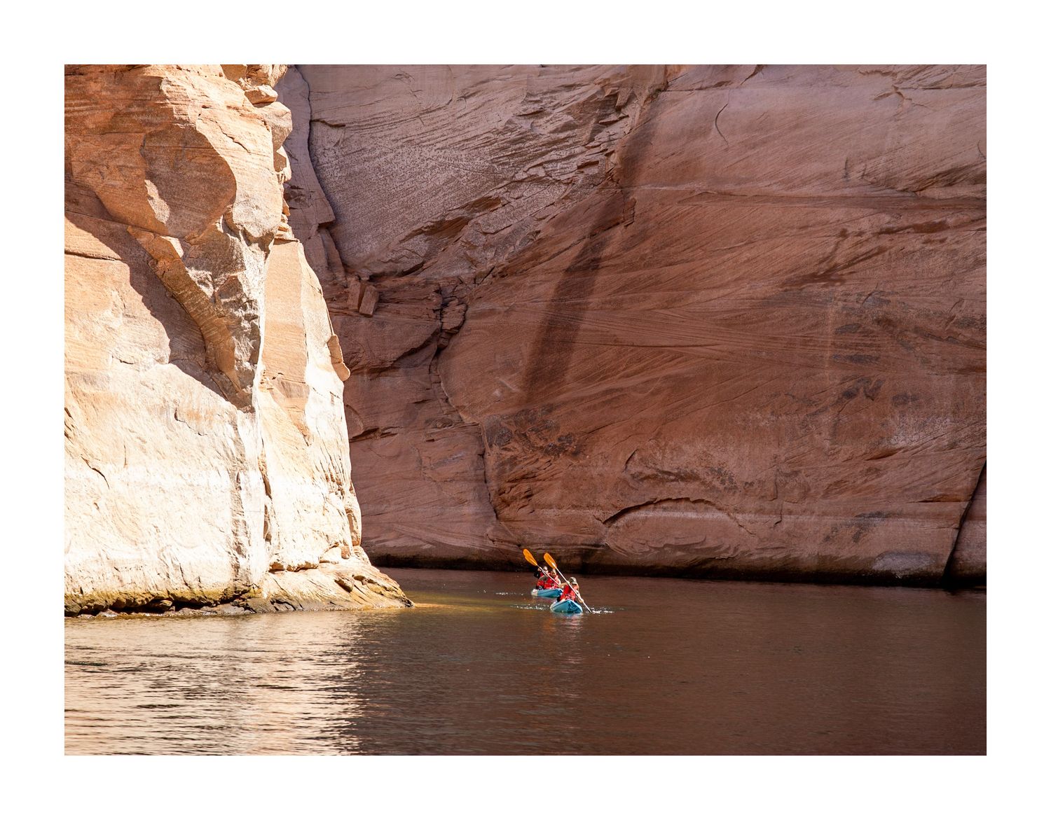 Kayaker paddling through narrow red rock canyon walls on calm water.