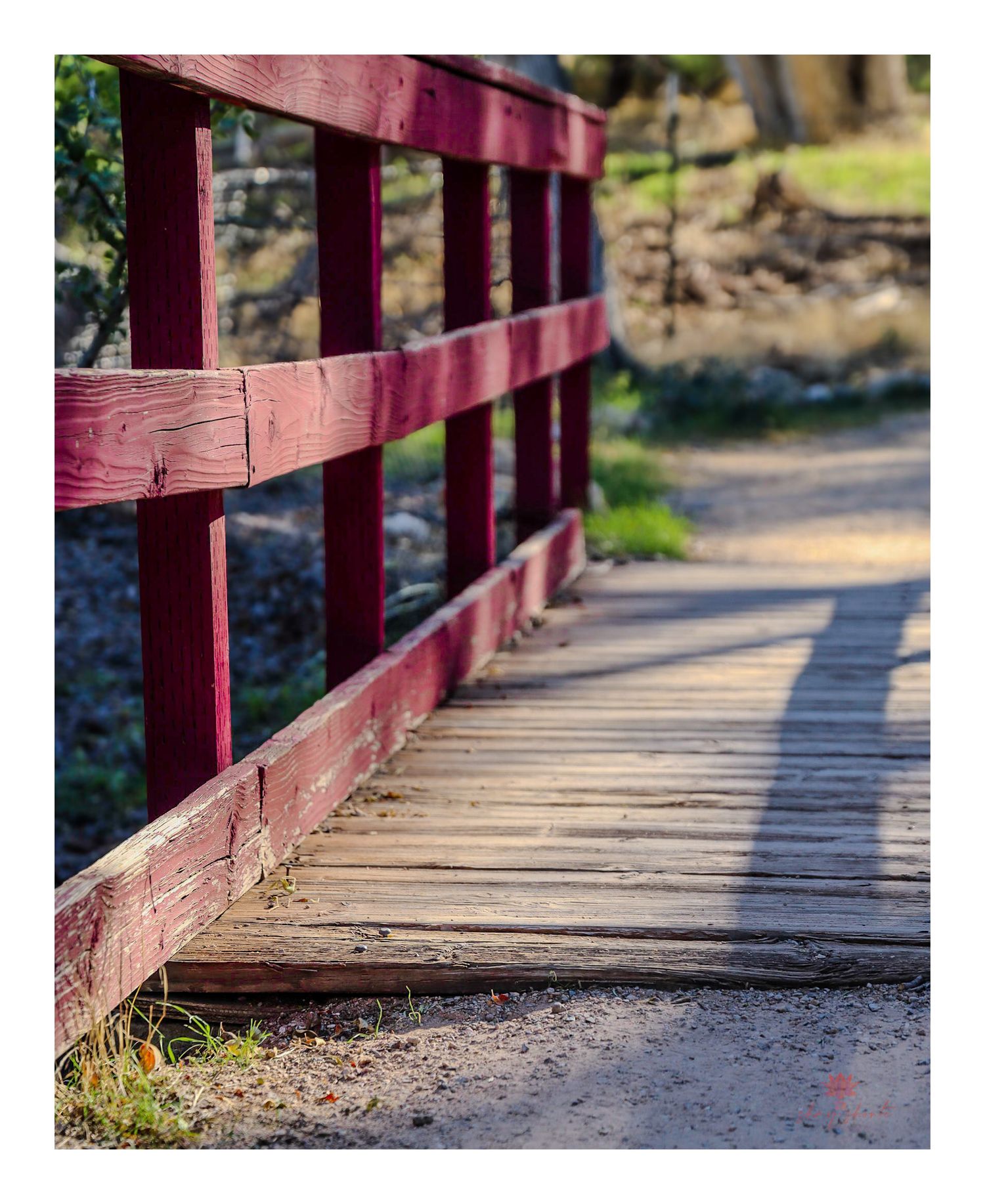 Red wooden bridge railing with dramatic shadow patterns cast on walkway.
