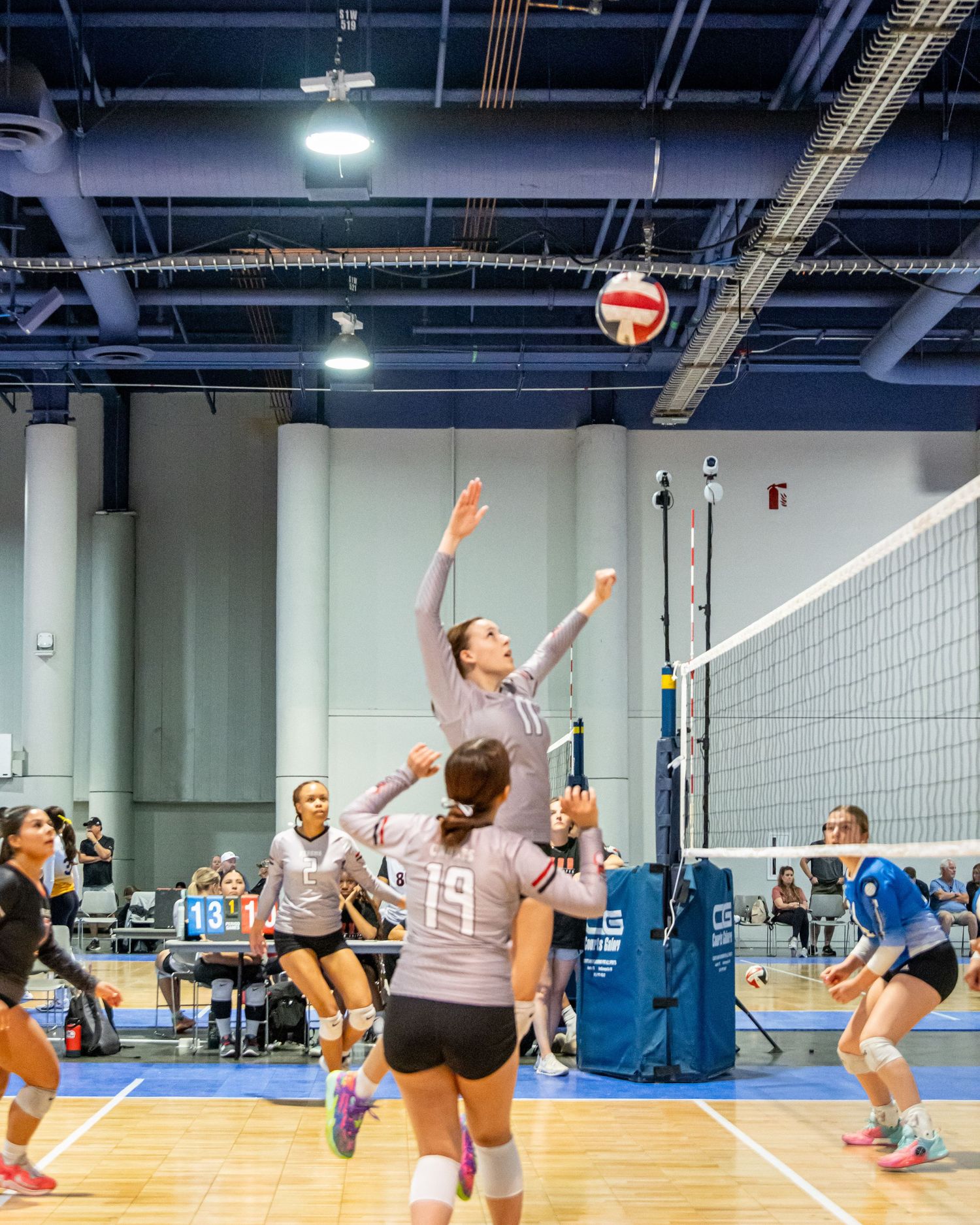 Competitive volleyball match in progress with players jumping to hit the ball over the net.