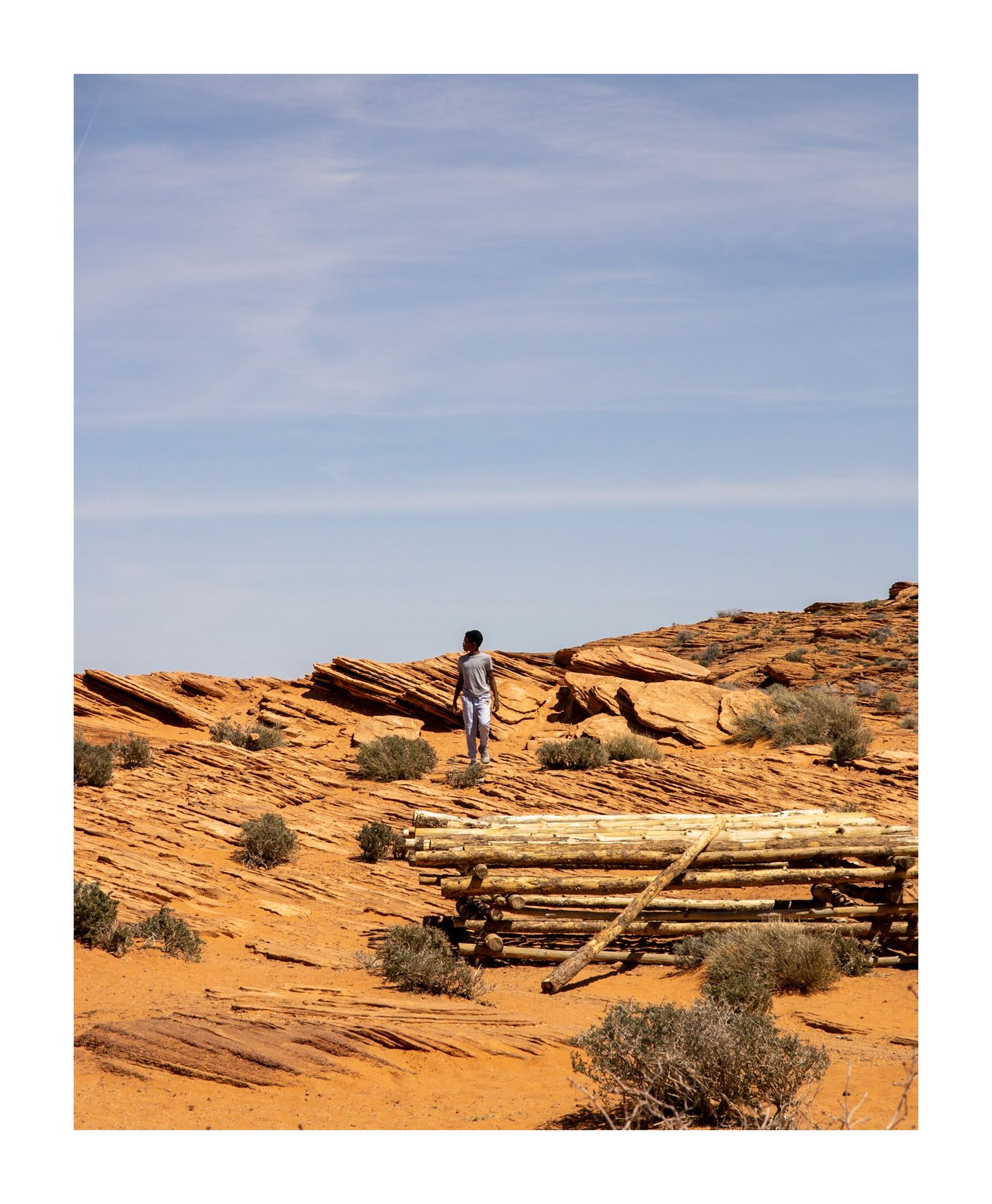 Desert landscape with red rock formations and scattered vegetation under blue sky.